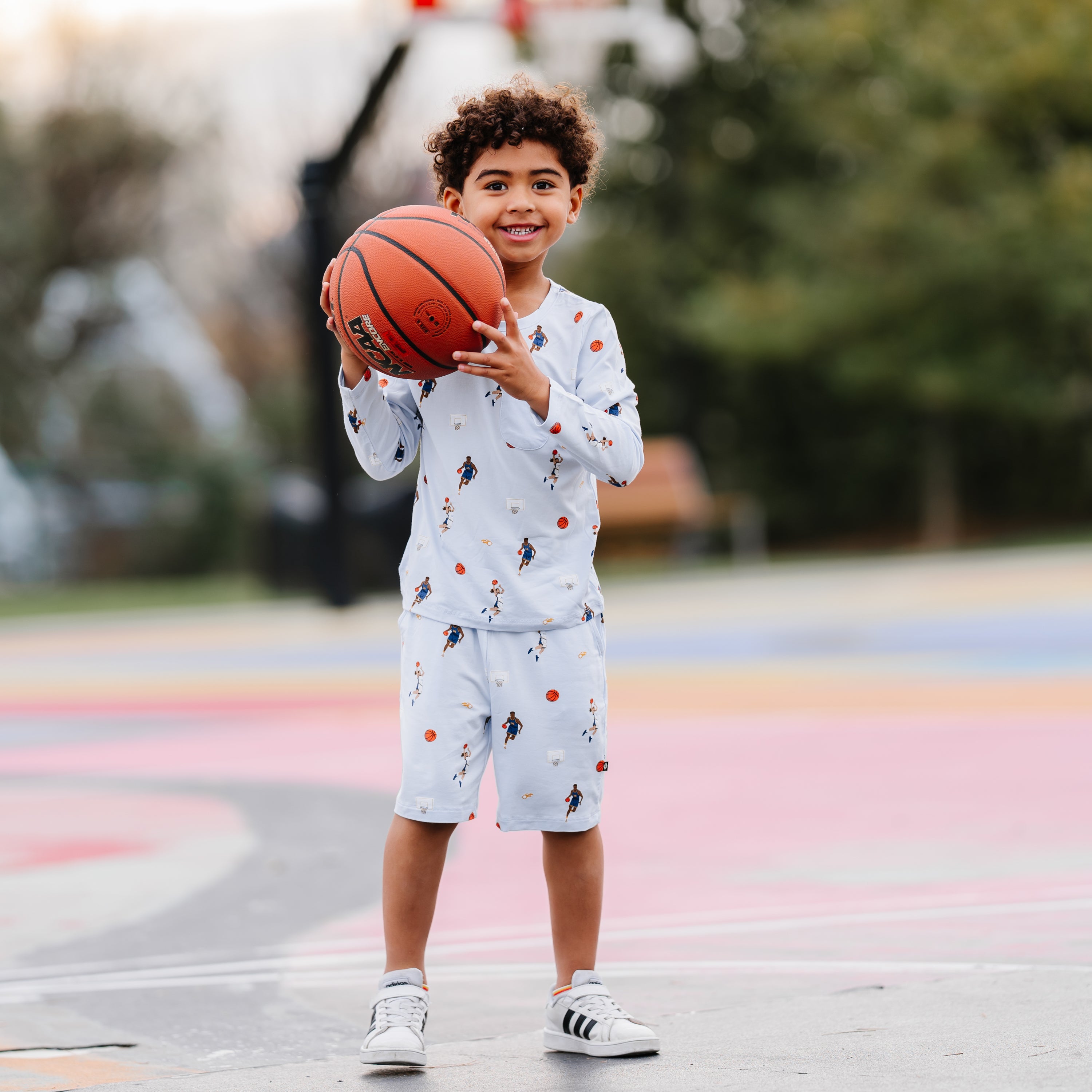 Young boy holding a basketball standing on a basketball court wearing the Long Sleeve Toddler Crew Neck Tee in Basketball and matching drawstring shorts
