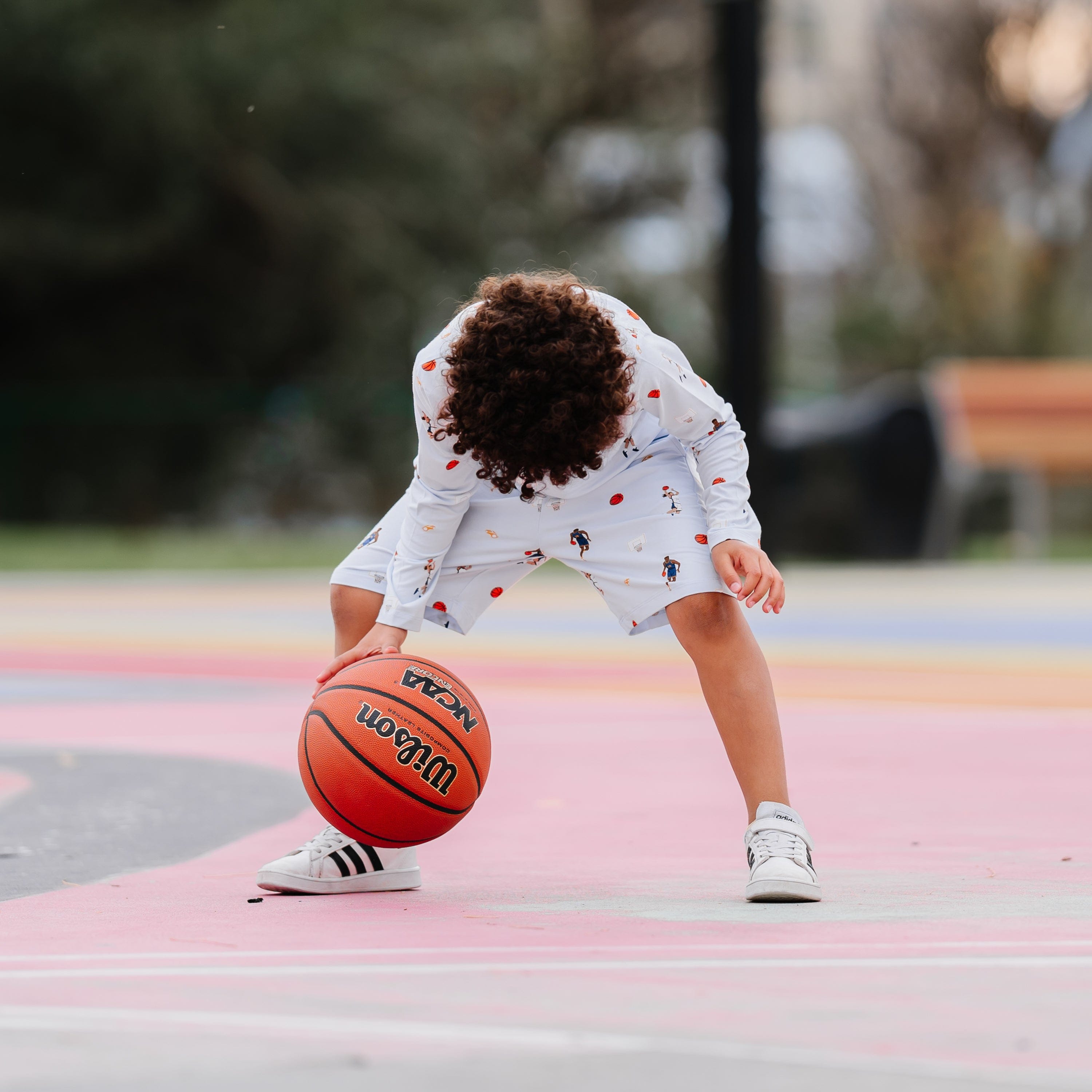 Young boy dribbling a basketball on a basketball court wearing the Drawstring Short in Basketball and matching long sleeve screw neck