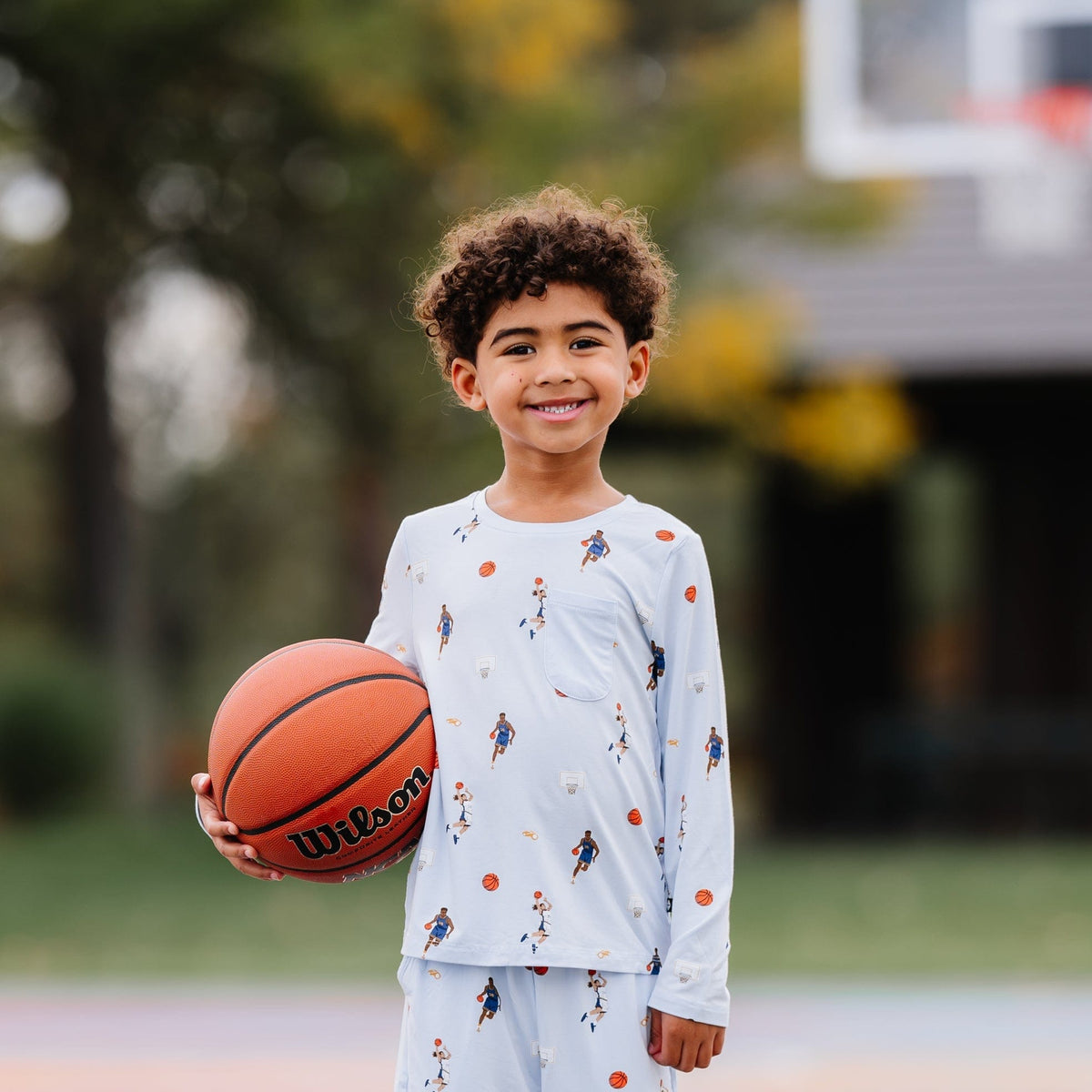 Young boy holding a basketball wearing the Long Sleeve Toddler Crew Neck Tee in Basketball