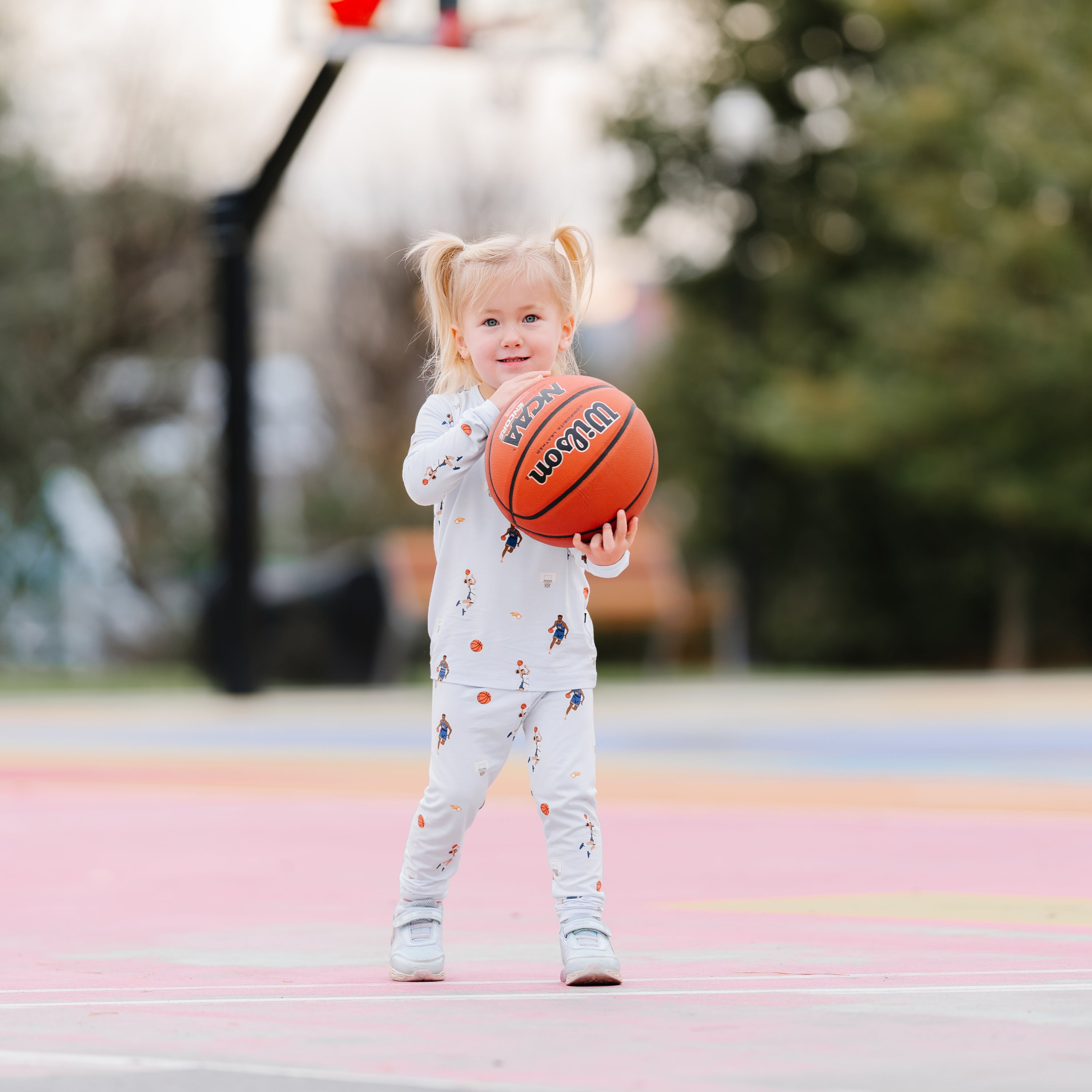 Young girl standing on a basketball court wearing the Long Sleeve Pajamas in Basketball holding a basketball