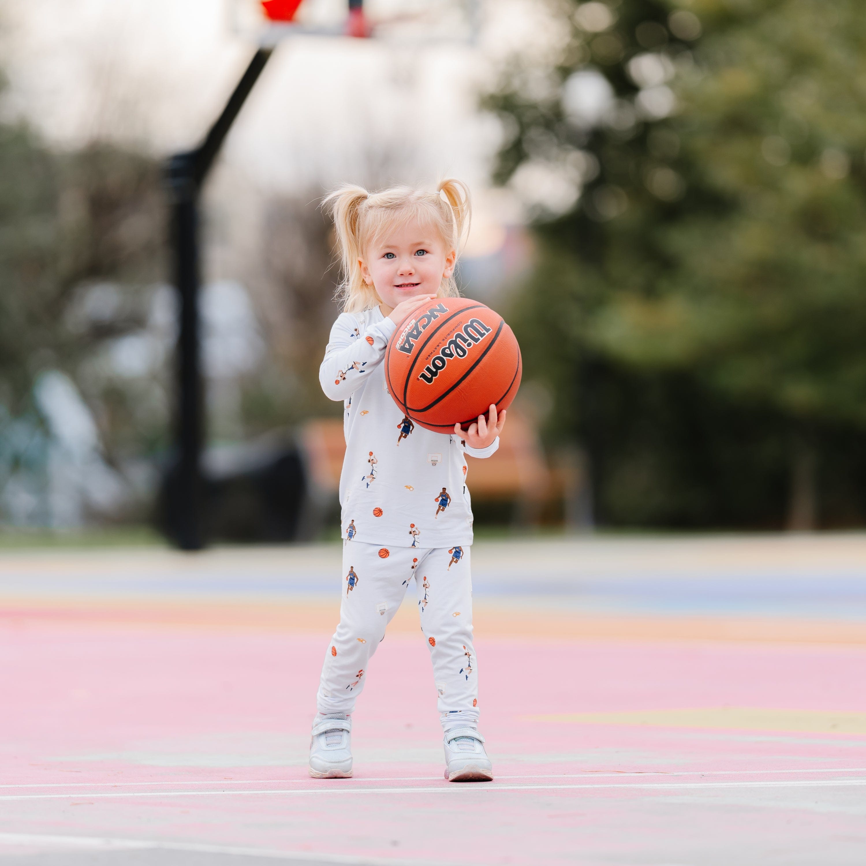 Young girl standing on a basketball court wearing the Long Sleeve Pajamas in Basketball holding a basketball