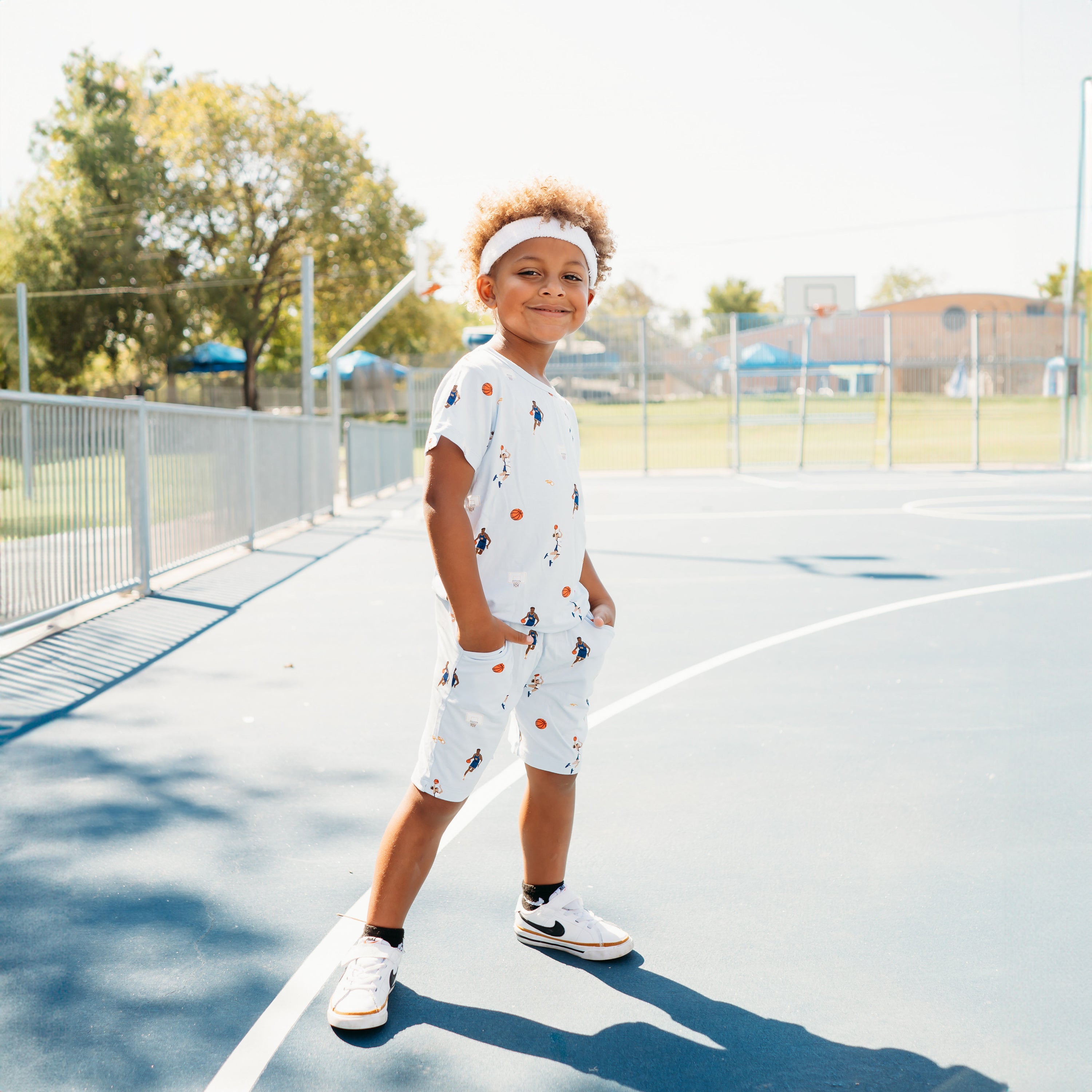Young boy standing on a basketball court with both hands in the pocket of the Drawstring Short in Basketball wearing a matching basic tee and white headband