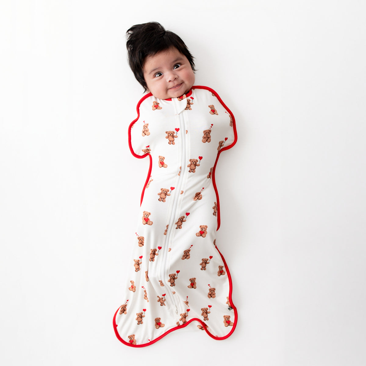 Newborn laying on a white surface wearing the Swaddle Bag in Bear Hearts 0.5