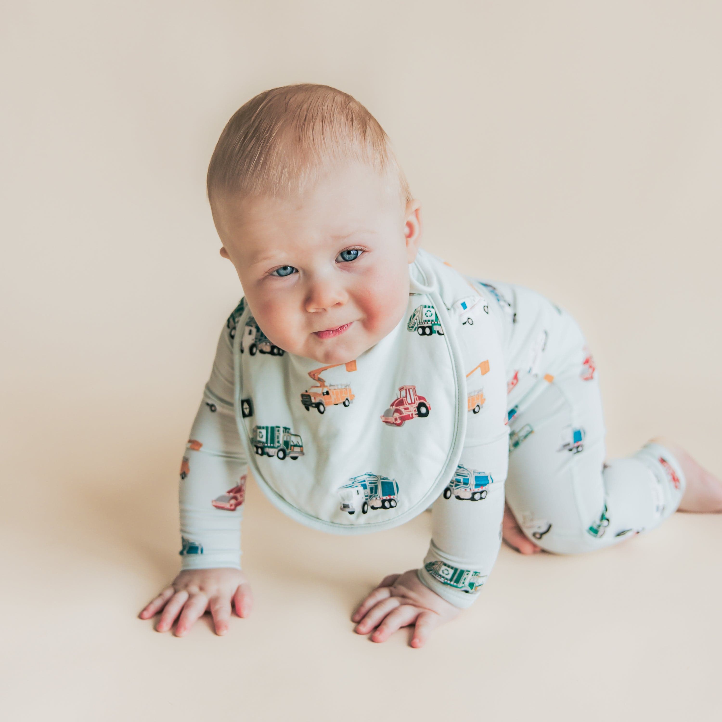 Toddler crawling wearing the soft and plush Cushy Bib in City Vehicles with a matching zippered romper