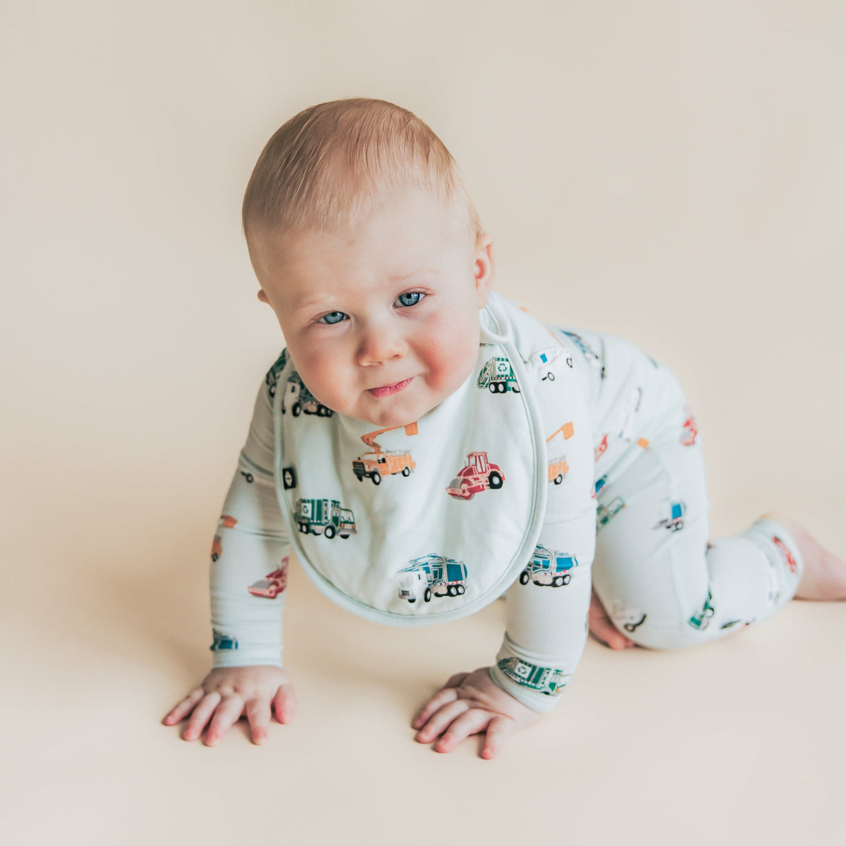 Toddler crawling wearing the soft and plush Cushy Bib in City Vehicles with a matching zippered romper