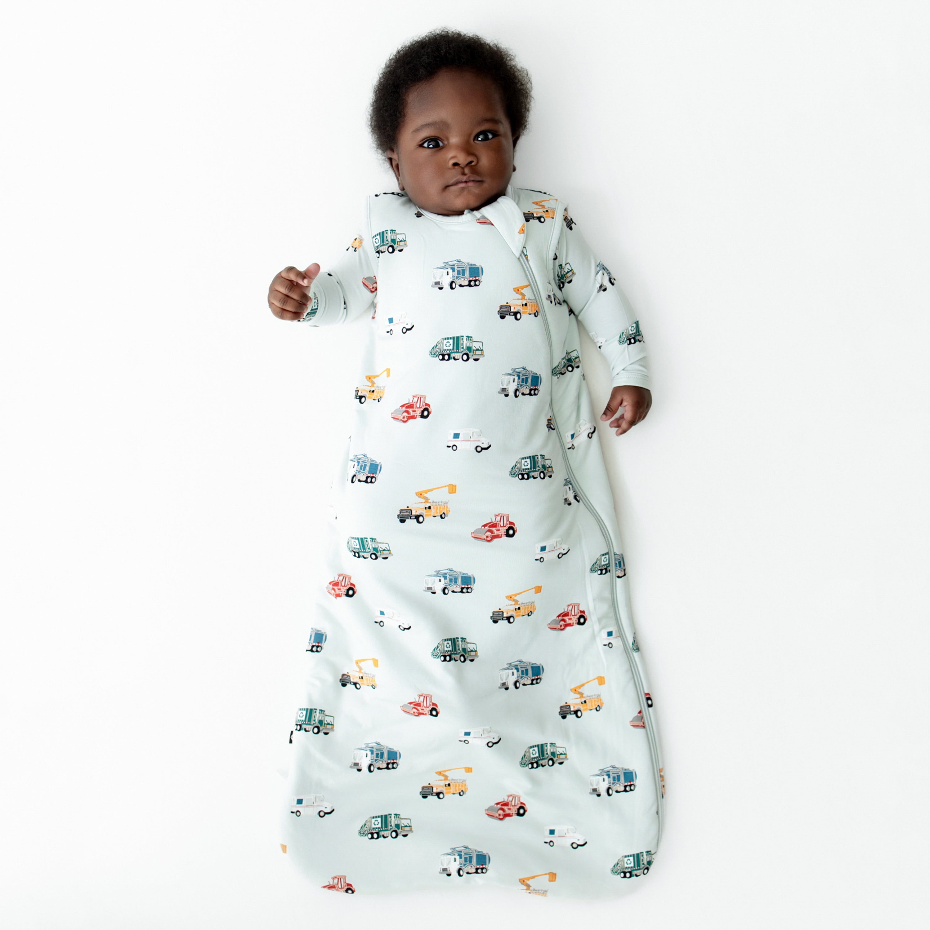 Young infant laying on a white surface wearing the soft and breathable Sleep Bag in City Vehicles 1.0 with a matching romper on underneath