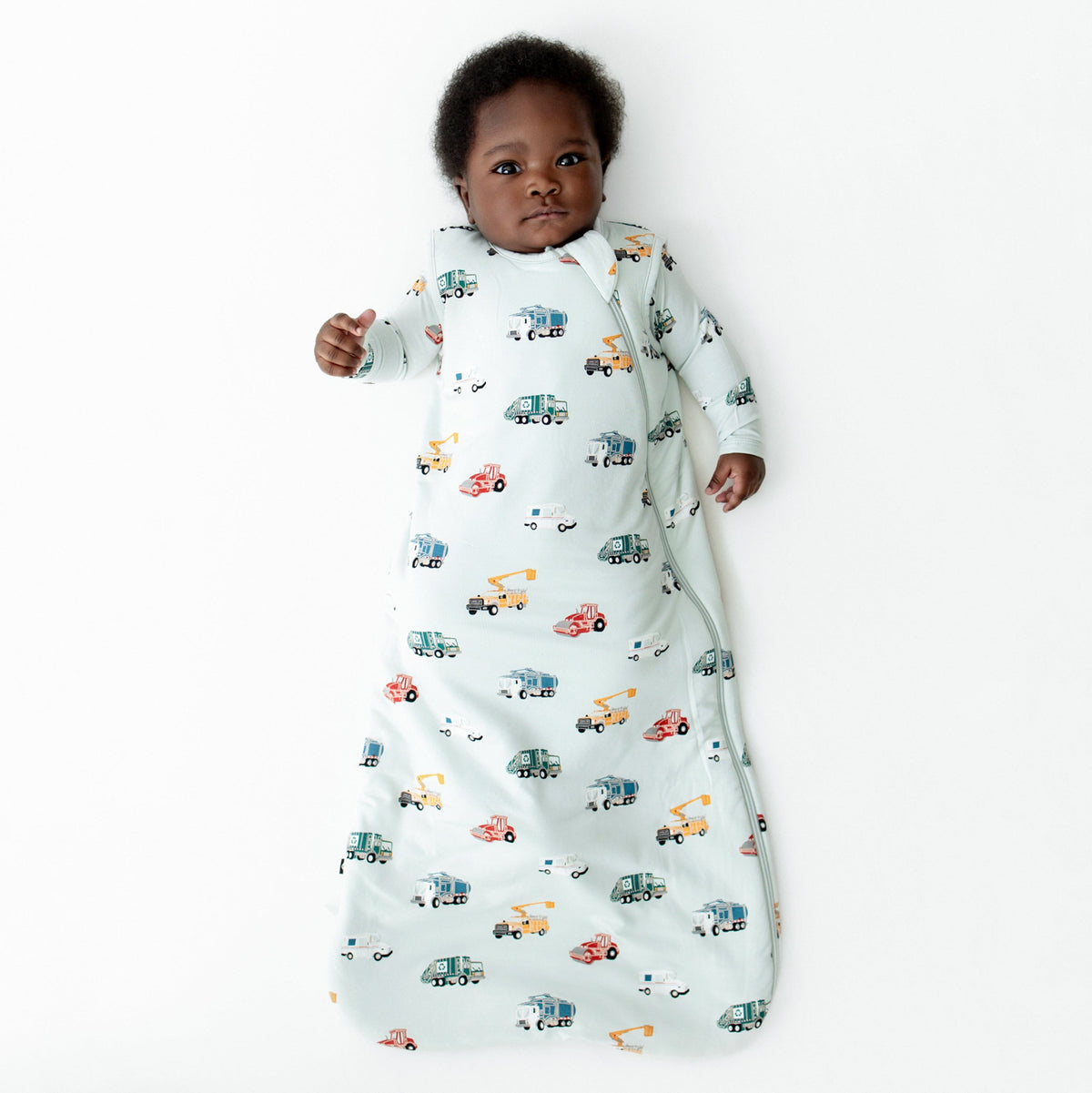 Young infant laying on a white surface wearing the soft and breathable Sleep Bag in City Vehicles 1.0 with a matching romper on underneath
