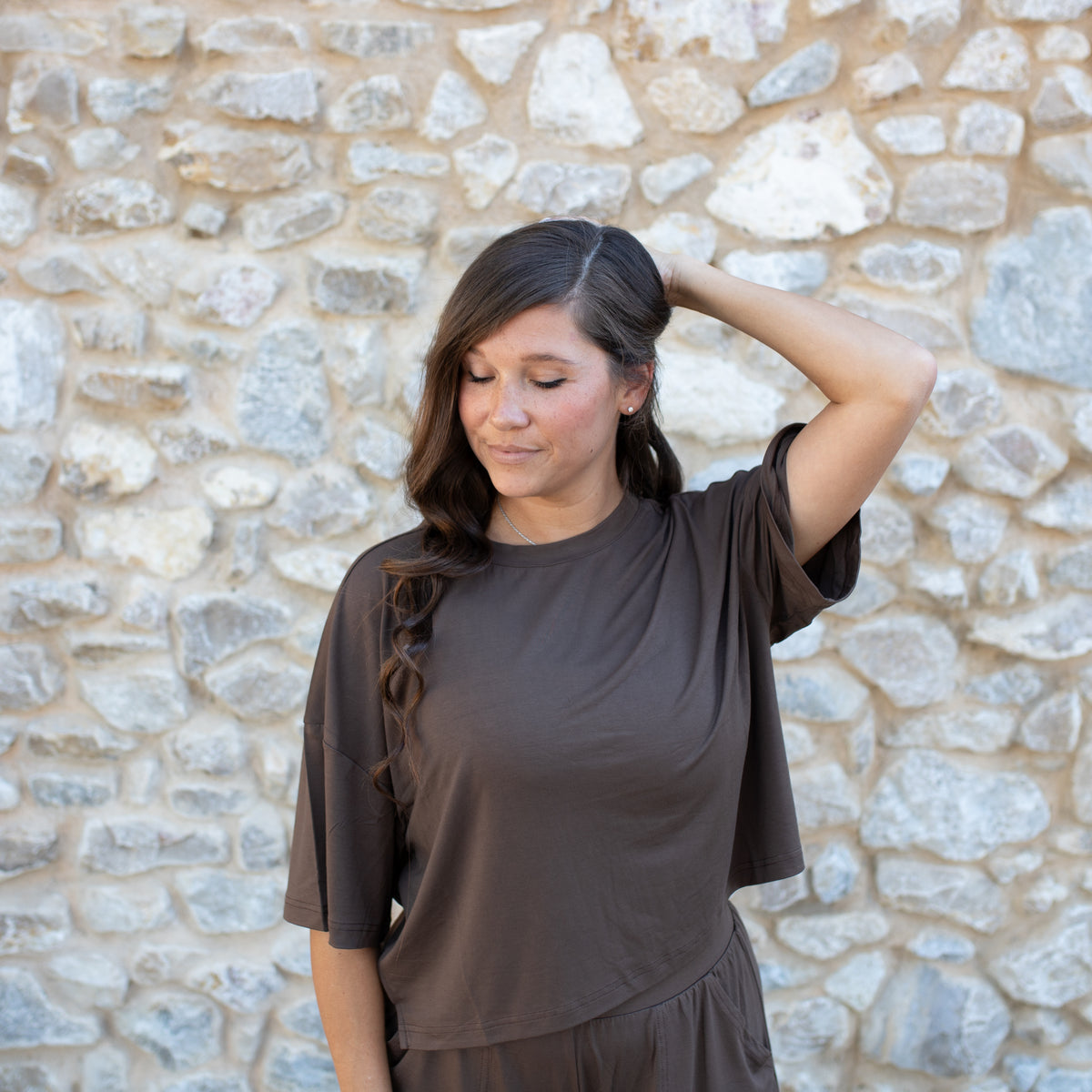 Woman wearing a brown top standing in front of a stone wall