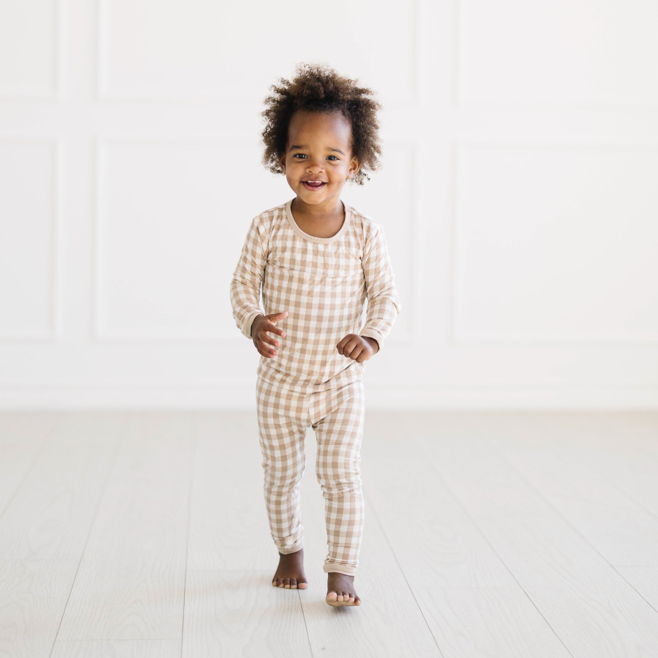 Young toddler walking wearing the Long Sleeve Pajamas in Gingham Bisque