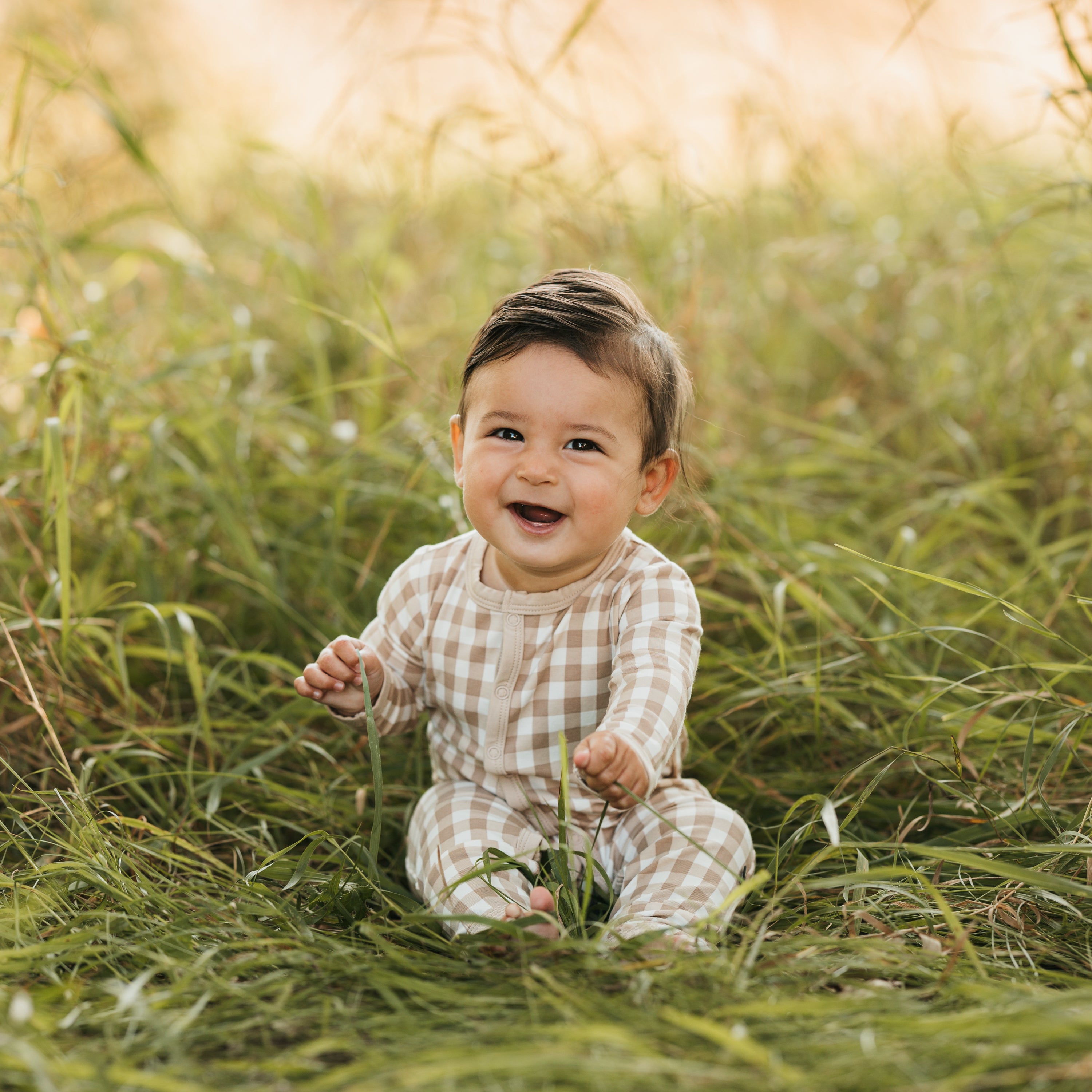 Infant sitting in the grass wearing the Romper in Gingham Bisque