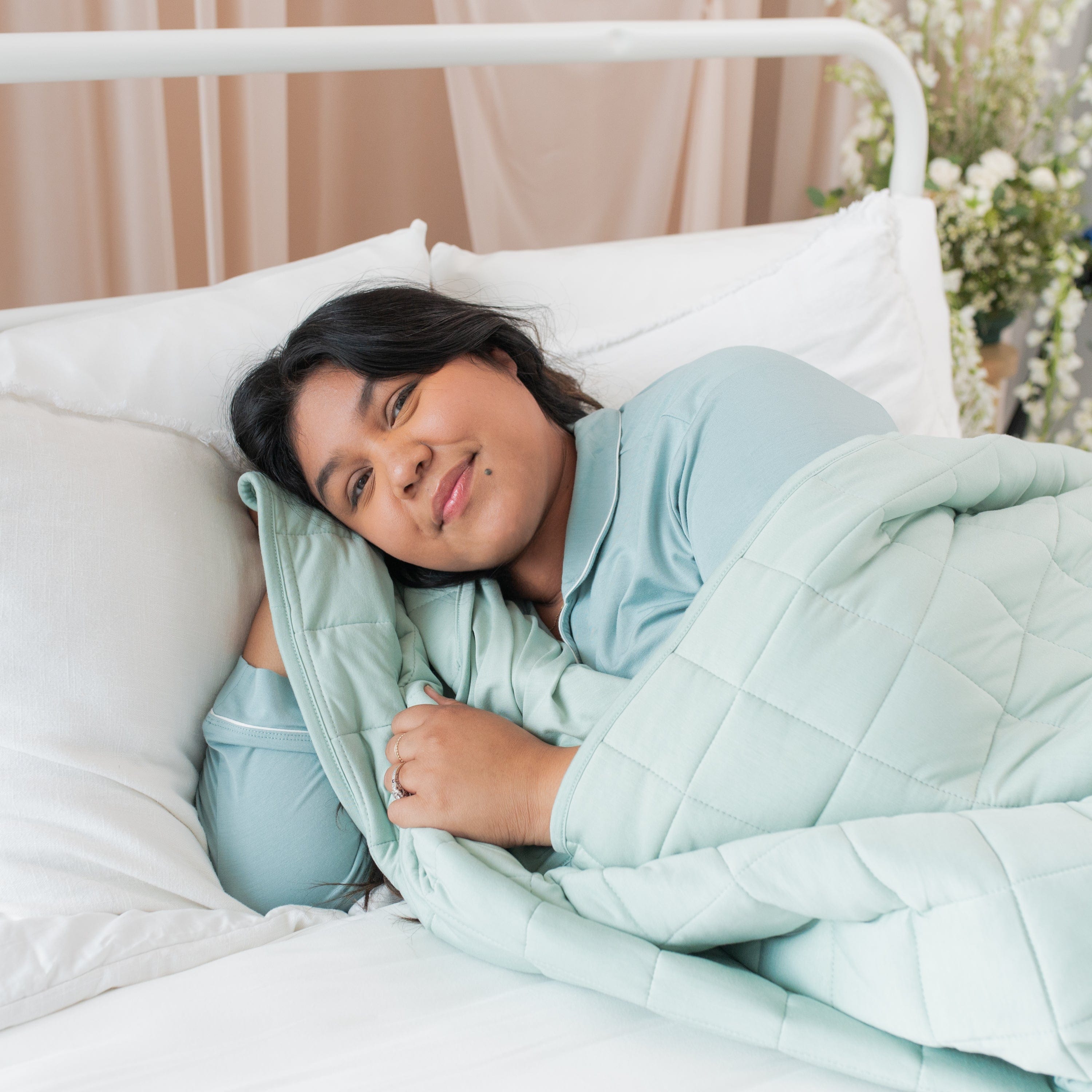 Woman laying in bed with Kyte Baby Adult Quilted Blanket in Sage 3.5