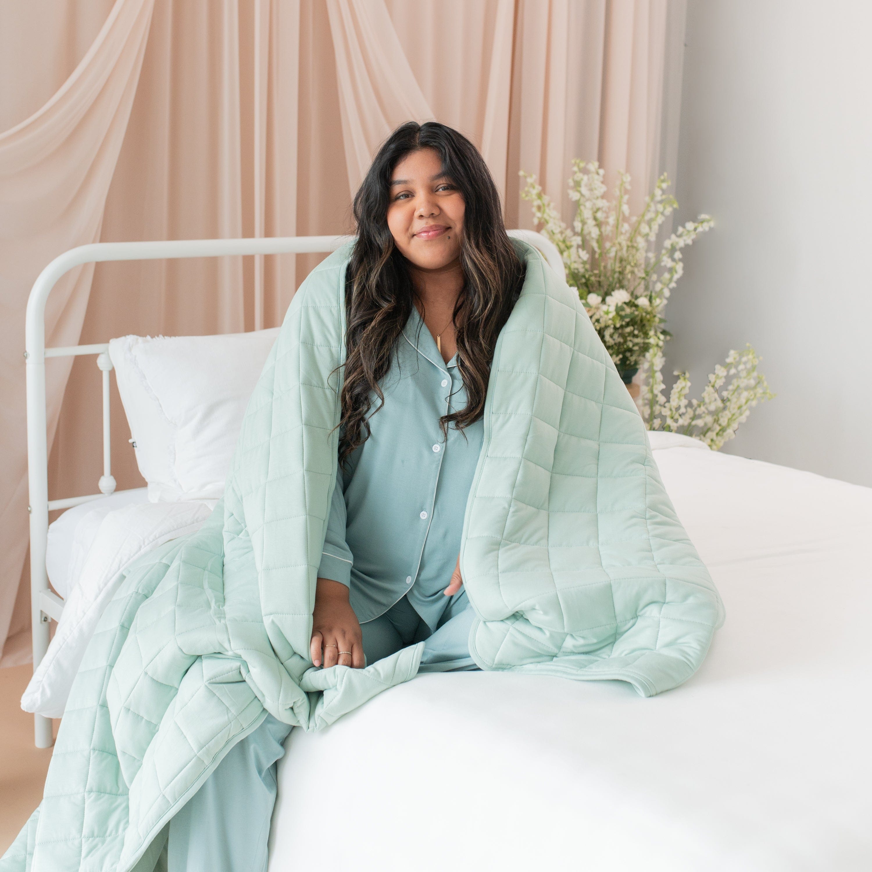 Woman wrapped in Kyte Baby Adult Quilted soft Blanket in Sage Green