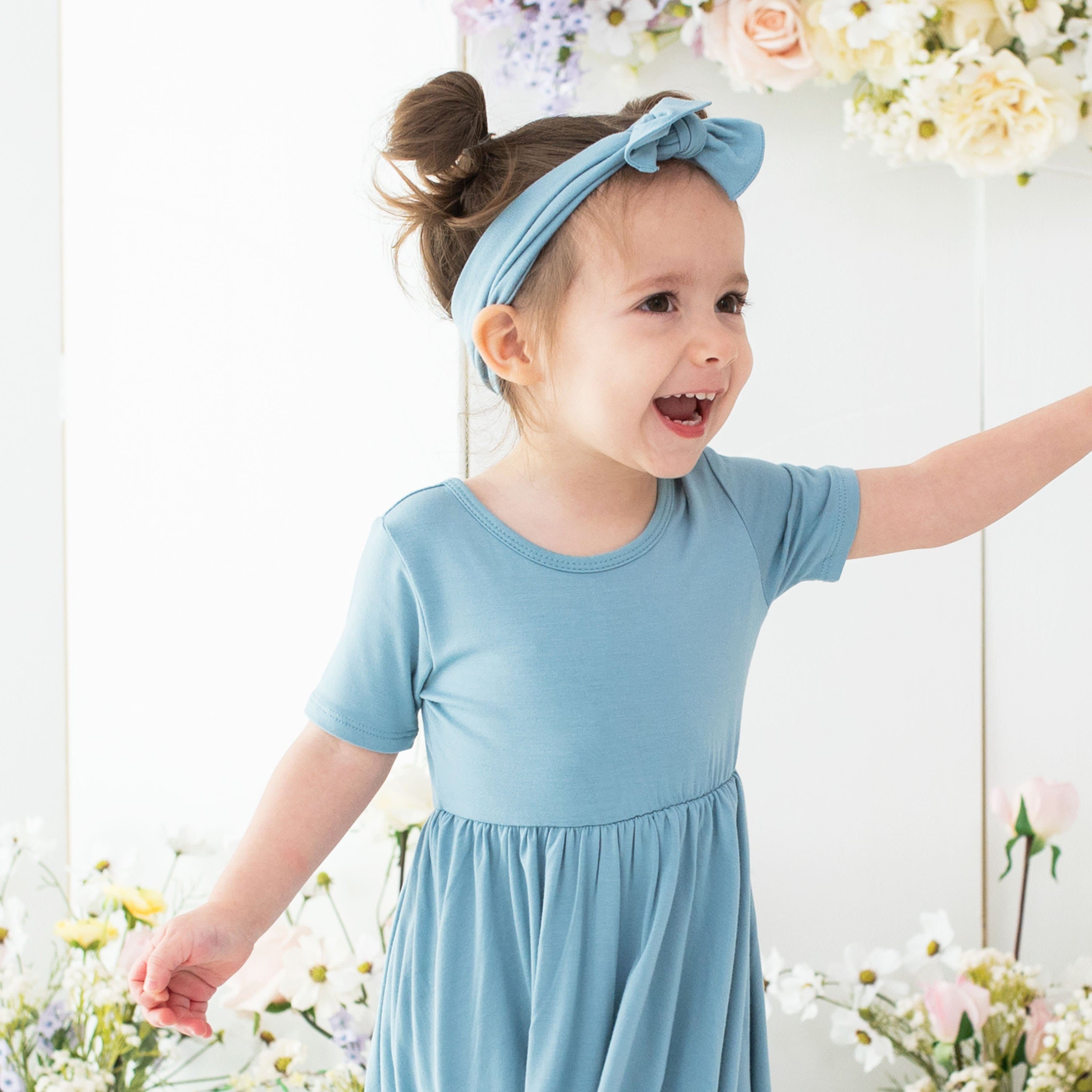 Toddler wearing Kyte Baby bamboo bow headband in Dusty Blue with matching dress