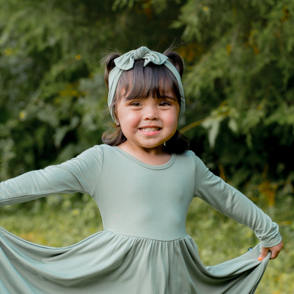 Young girl wearing the Knotted bow headband in Thyme paired with a matching long sleeve dress