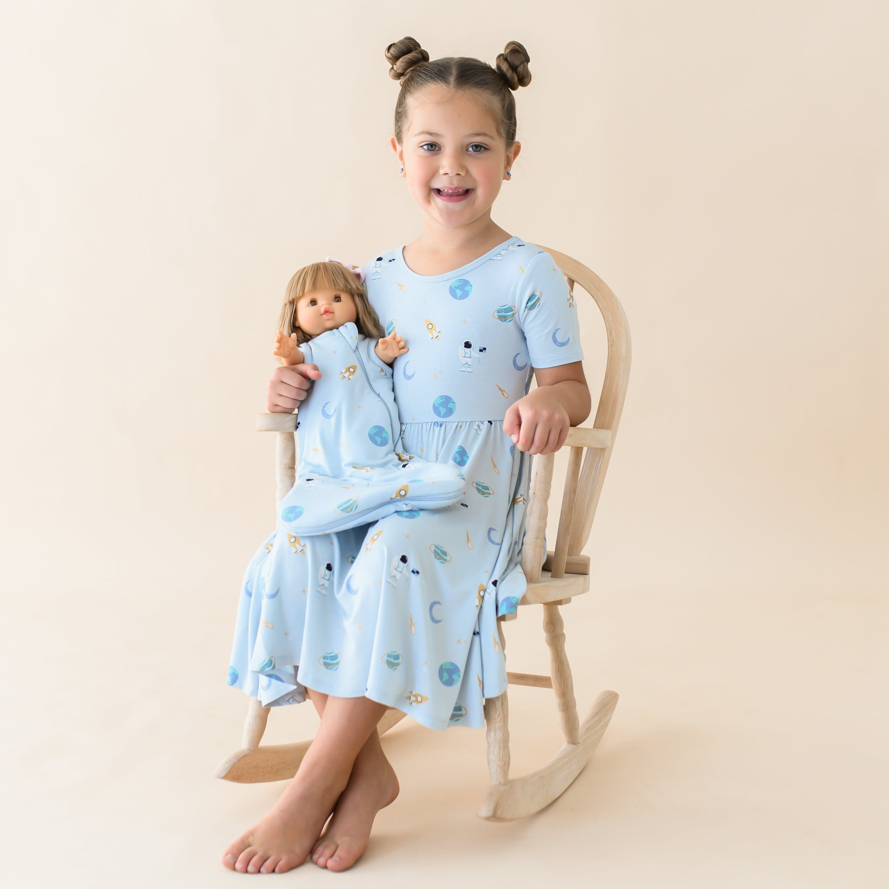 Girl wearing Kyte Baby Twirl Dress with toy in matching Baby Doll Sleep Bag in Ice Space