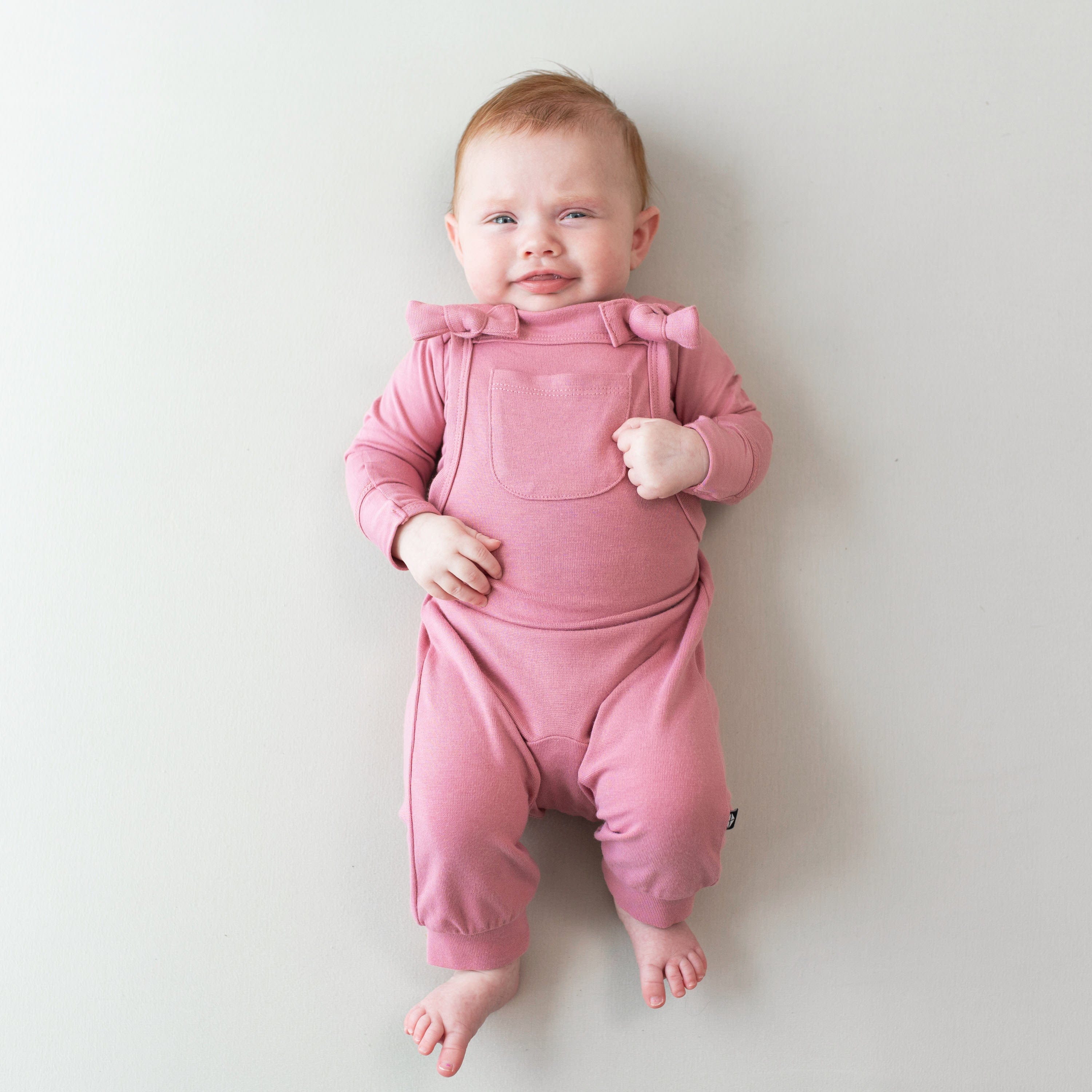 Infant wearing Kyte Baby Bamboo Jersey adjustable Overall in Apple Blossom pink