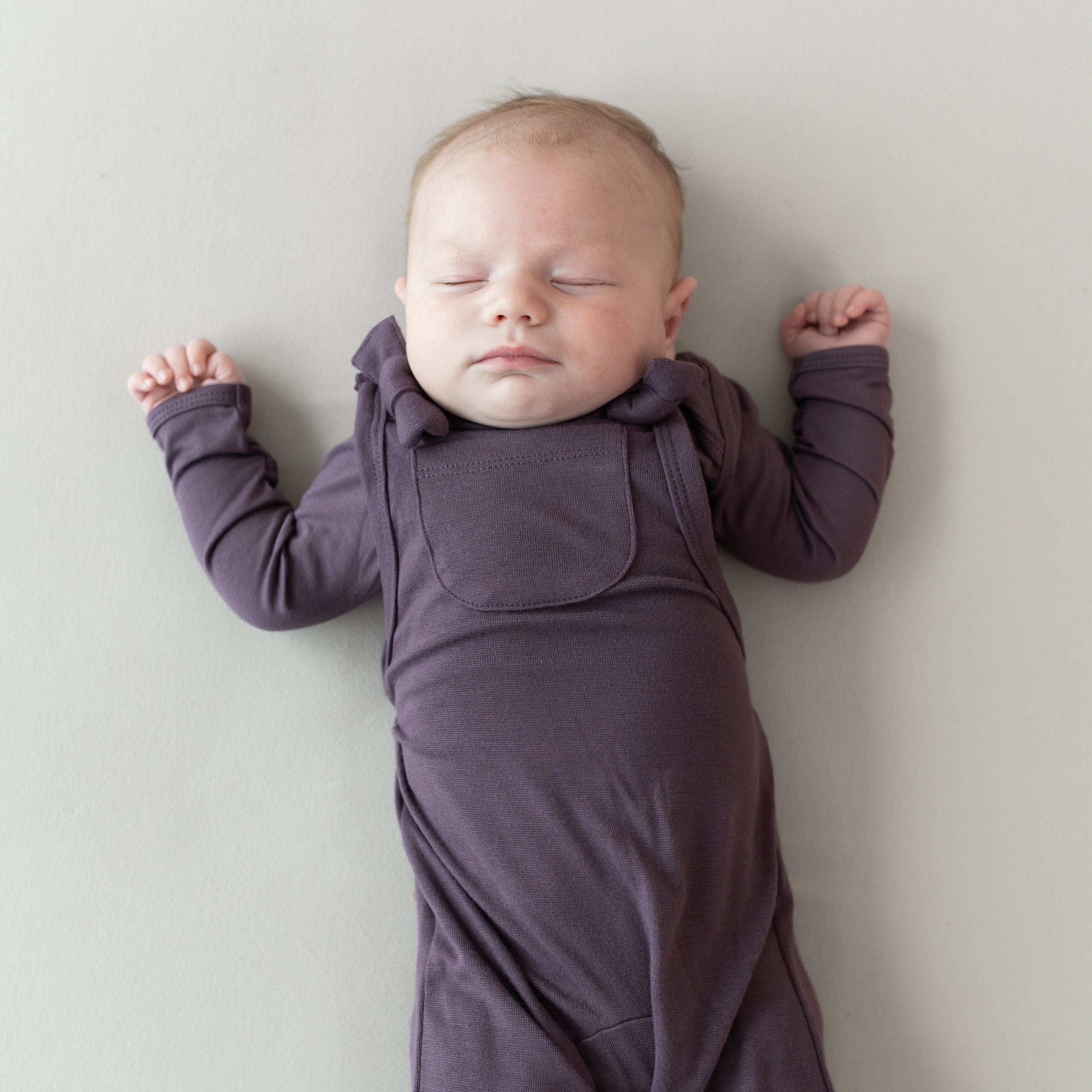 Infant wearing Kyte Baby Bamboo Jersey Overalls with front pocket in Currant purple