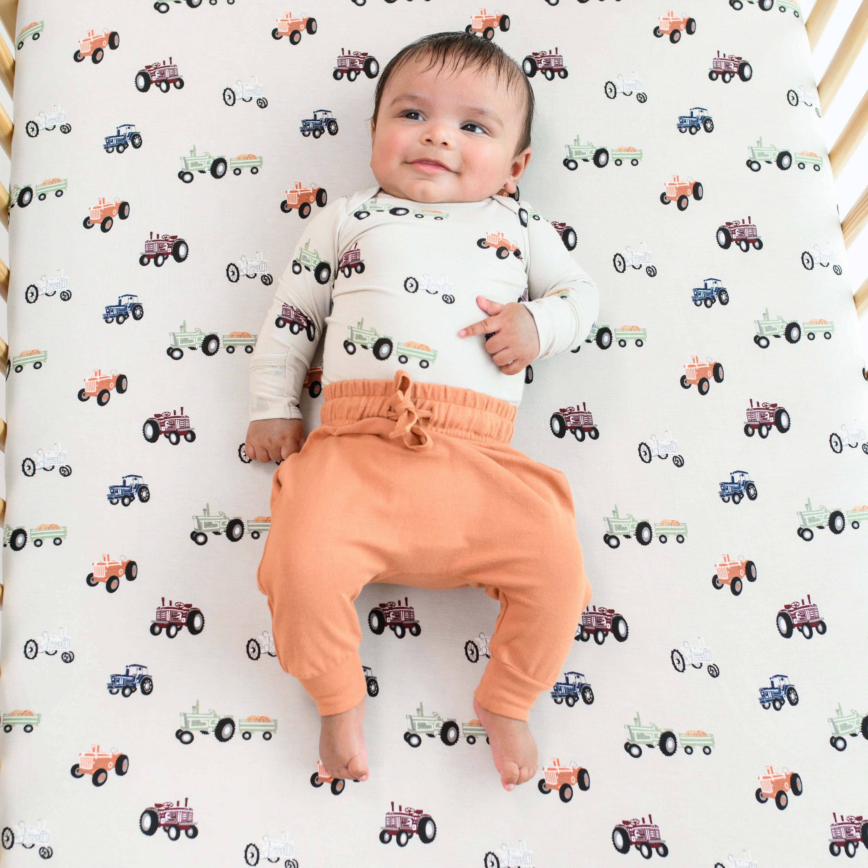 Infant wearing Kyte Baby Long Sleeve Bodysuit in Tractor with Bamboo Jersey Harem Pants in Apricot