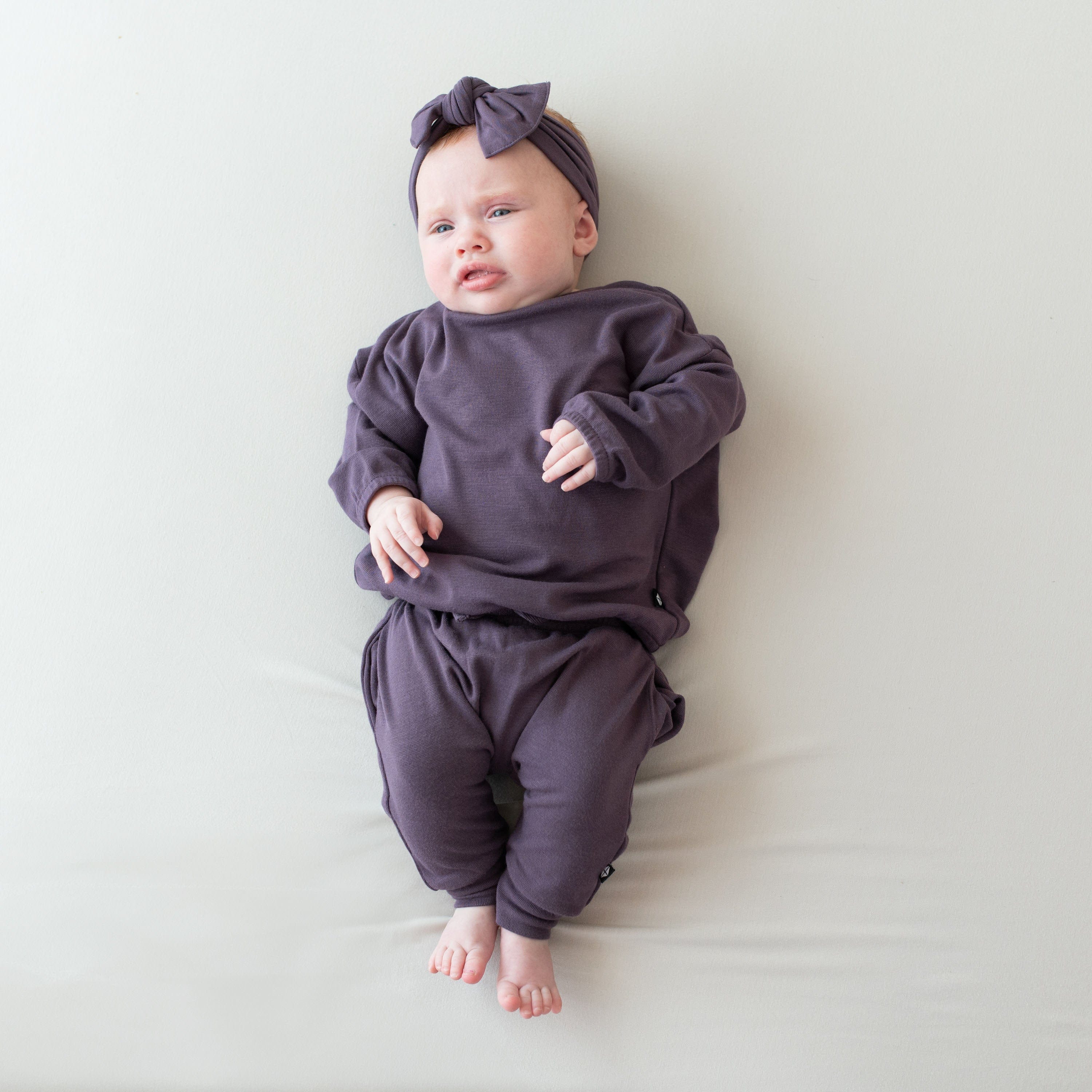 Infant wearing Kyte Baby Bamboo Jersey Long Sleeve Drop Shoulder Top and Harem Pants in Currant