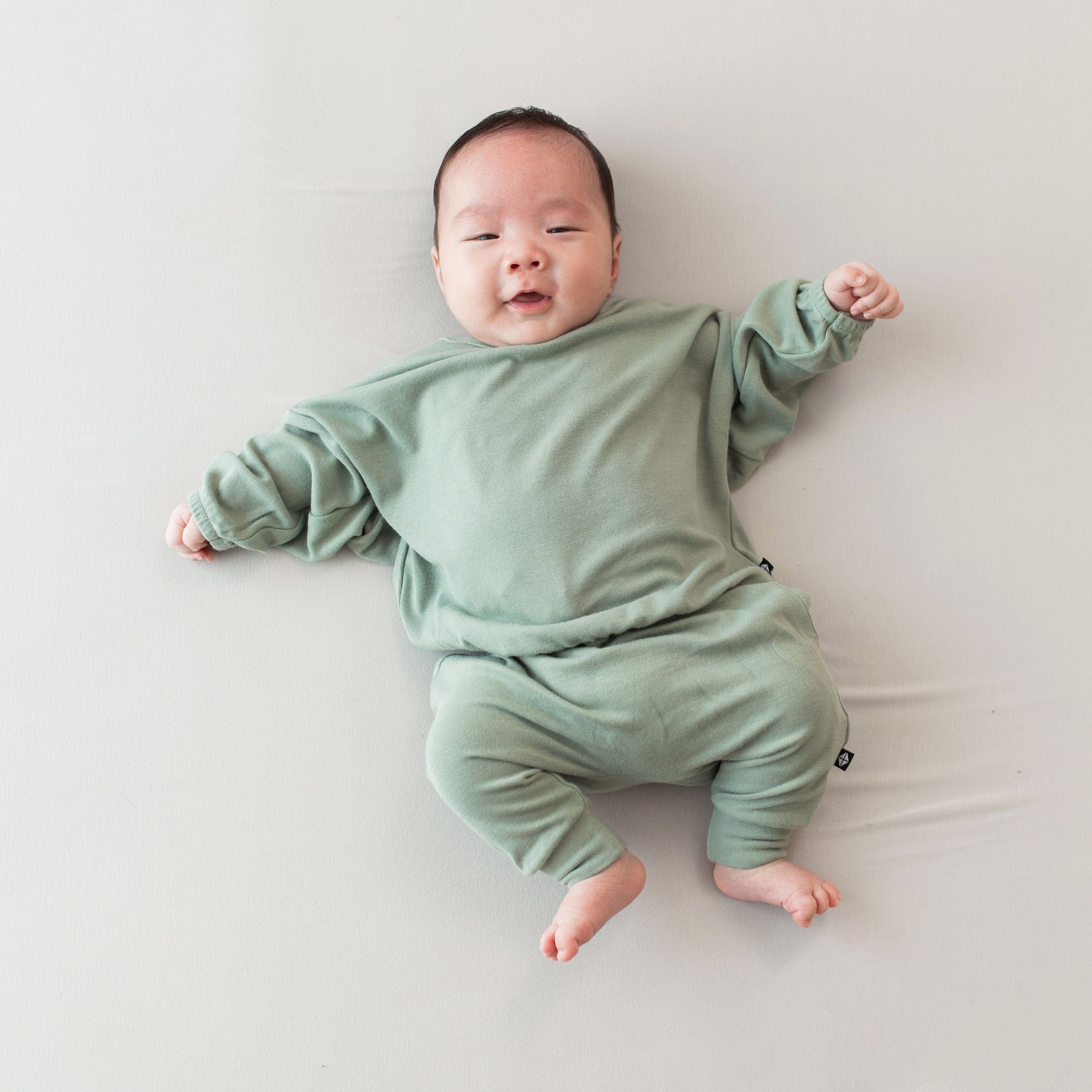 Infant wearing Kyte Baby Bamboo Jersey Long Sleeve Drop Shoulder Top and Harem Pants in Thyme