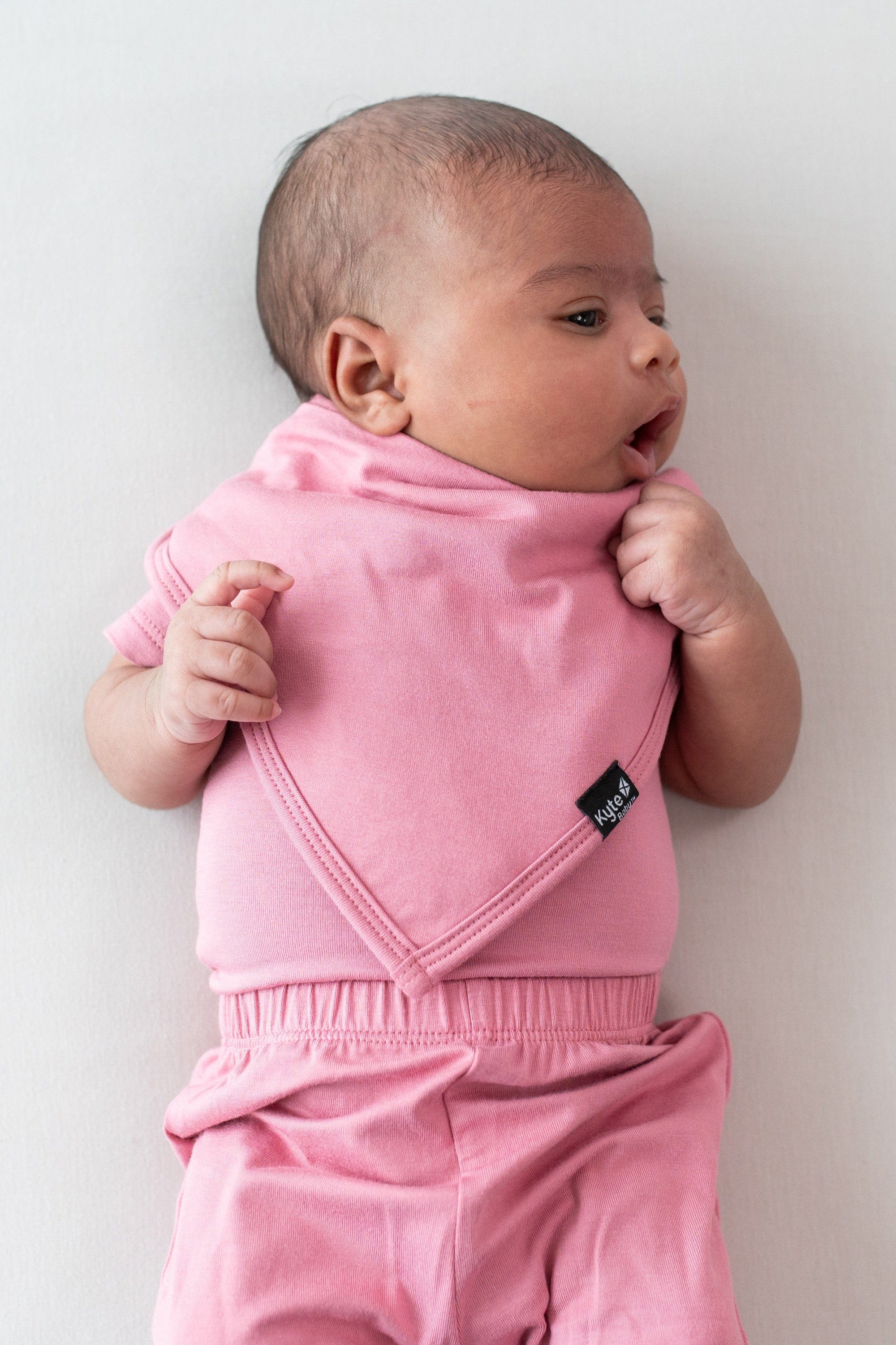 Newborn wearing Kyte Baby Bib in Apple Blossom with matching bodysuit and pant