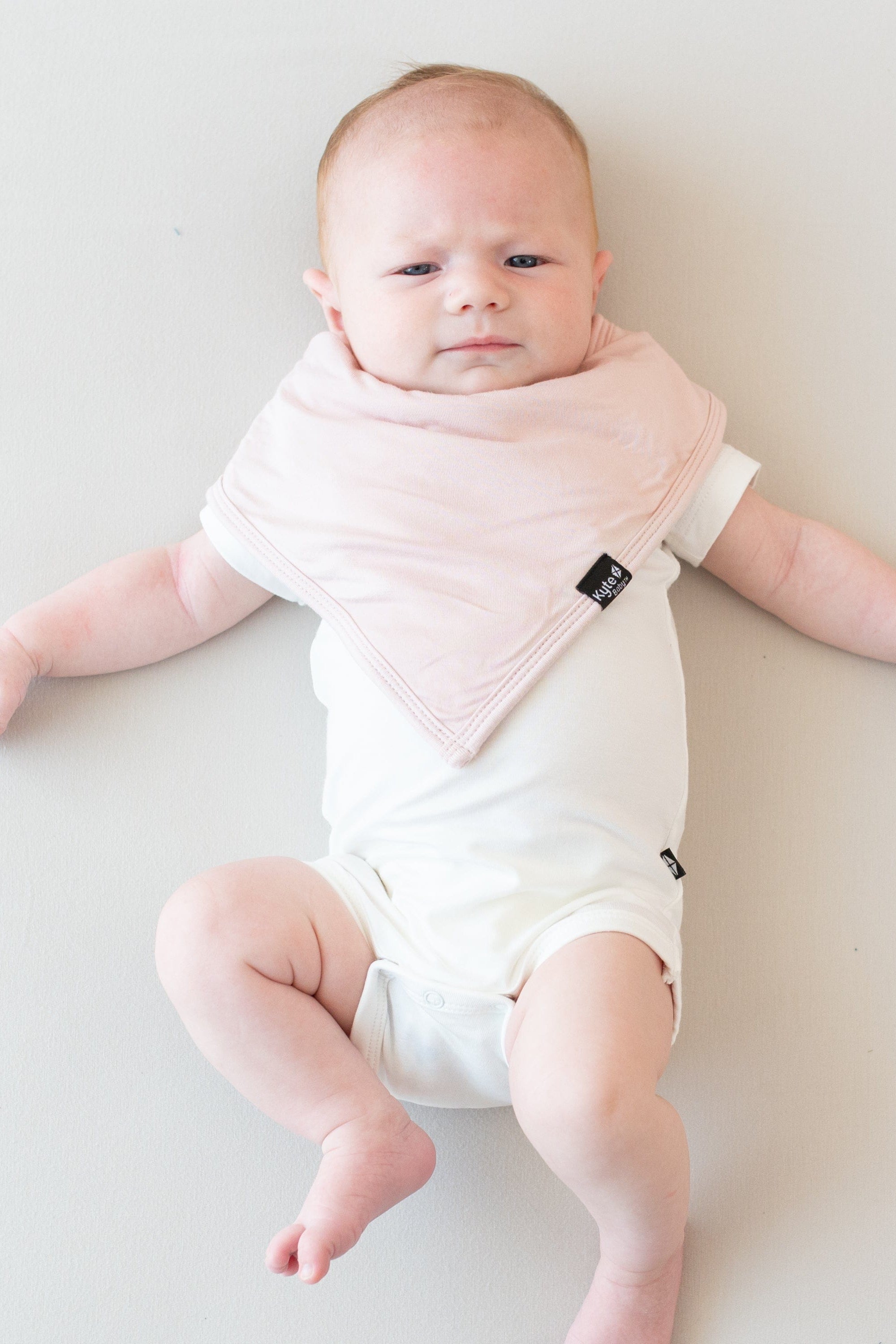Baby laying on an eggshell surface while modeling a Bib in Blush