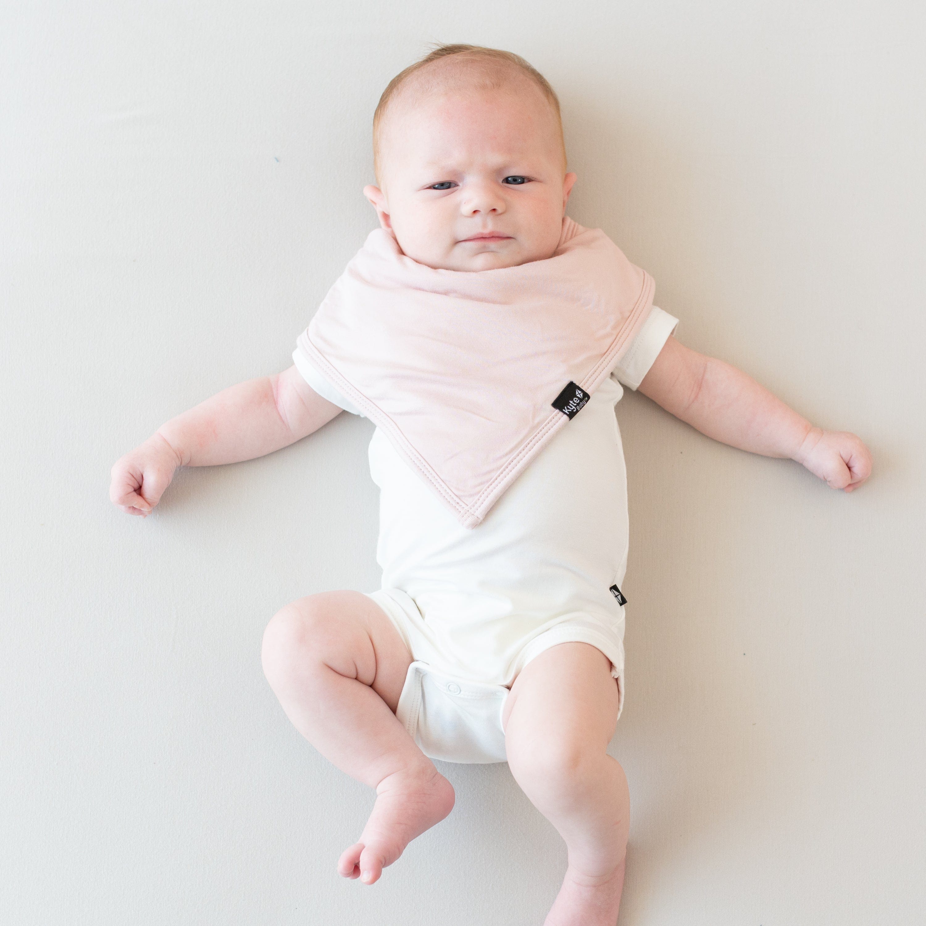 Baby laying on an eggshell surface while modeling a Bib in Blush