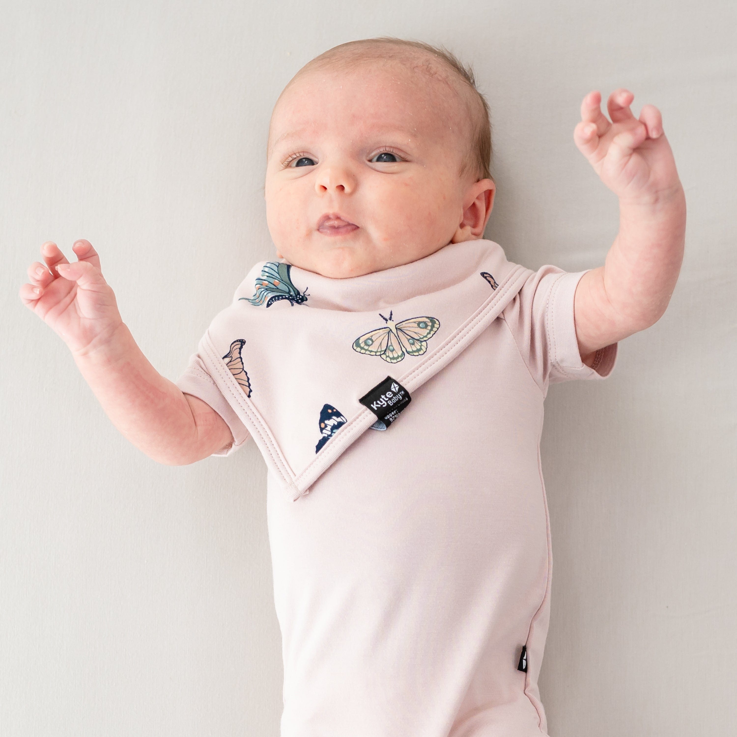 Infant laying down with hands in the air wearing the Bib in Blush Butterfly and Blush short sleeve bodysuit
