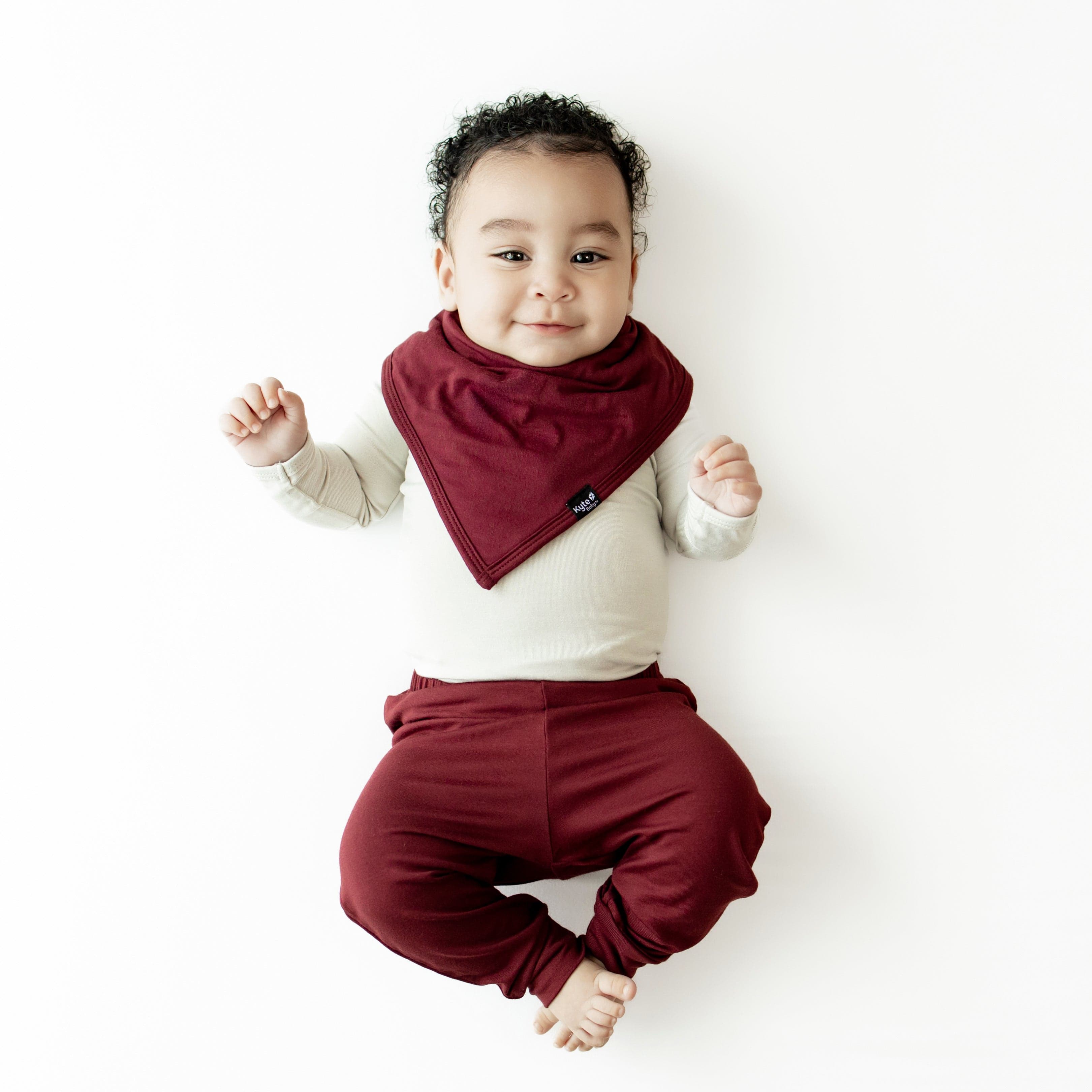 Infant wearing the Bib in Burgundy paired with matching pants and an Oat long sleeve bodysuit