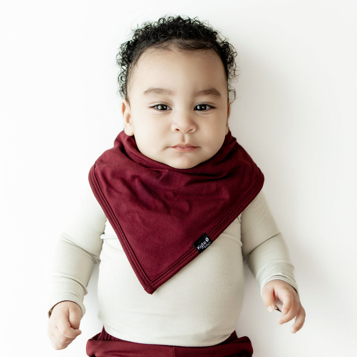 Infant wearing the Bib in Burgundy overtop an Oat long sleeve bodysuit