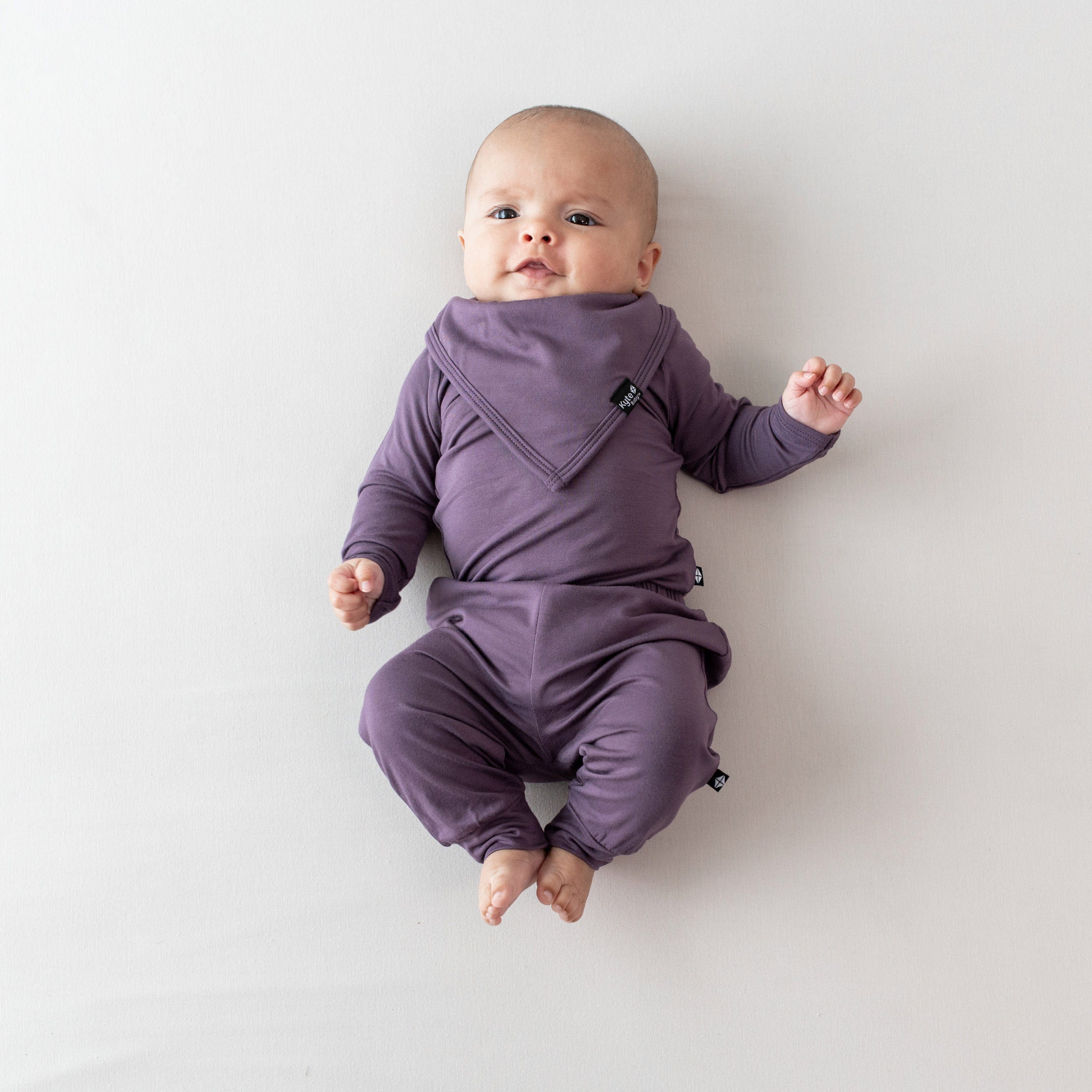 Infant laying on a a beige blanket wearing the Bib in Currant with matching long sleeve bodysuit and pants