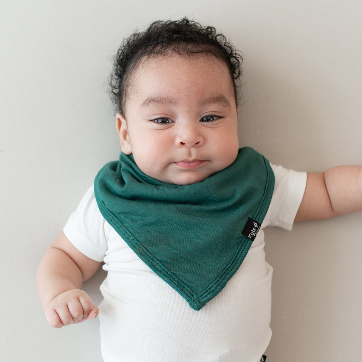 Infant wearing a Kyte Baby Bib in Emerald and Short Sleeve Bodysuit in Cloud