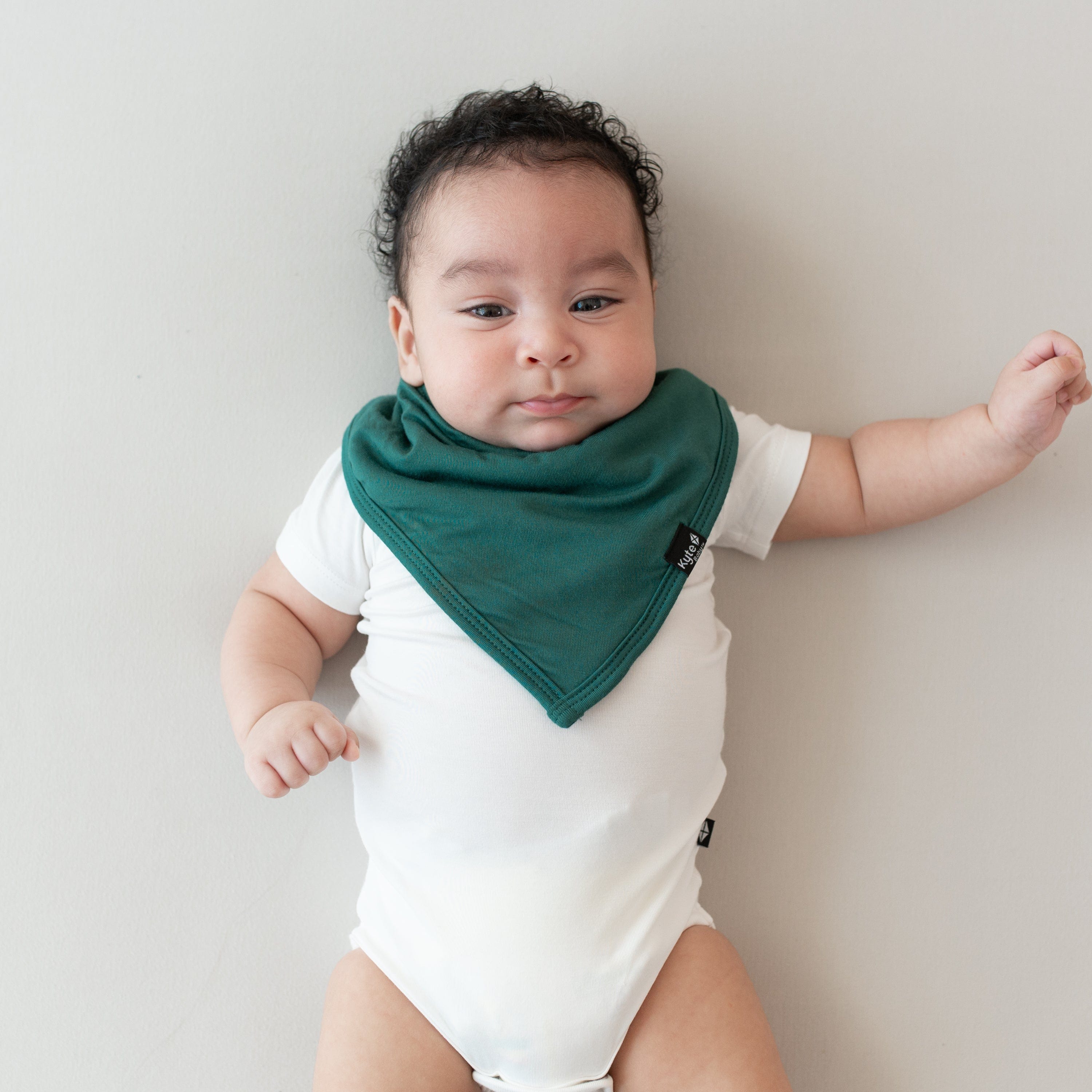 Infant laying on a Crib in Oat while wearing a Bib in Emerald