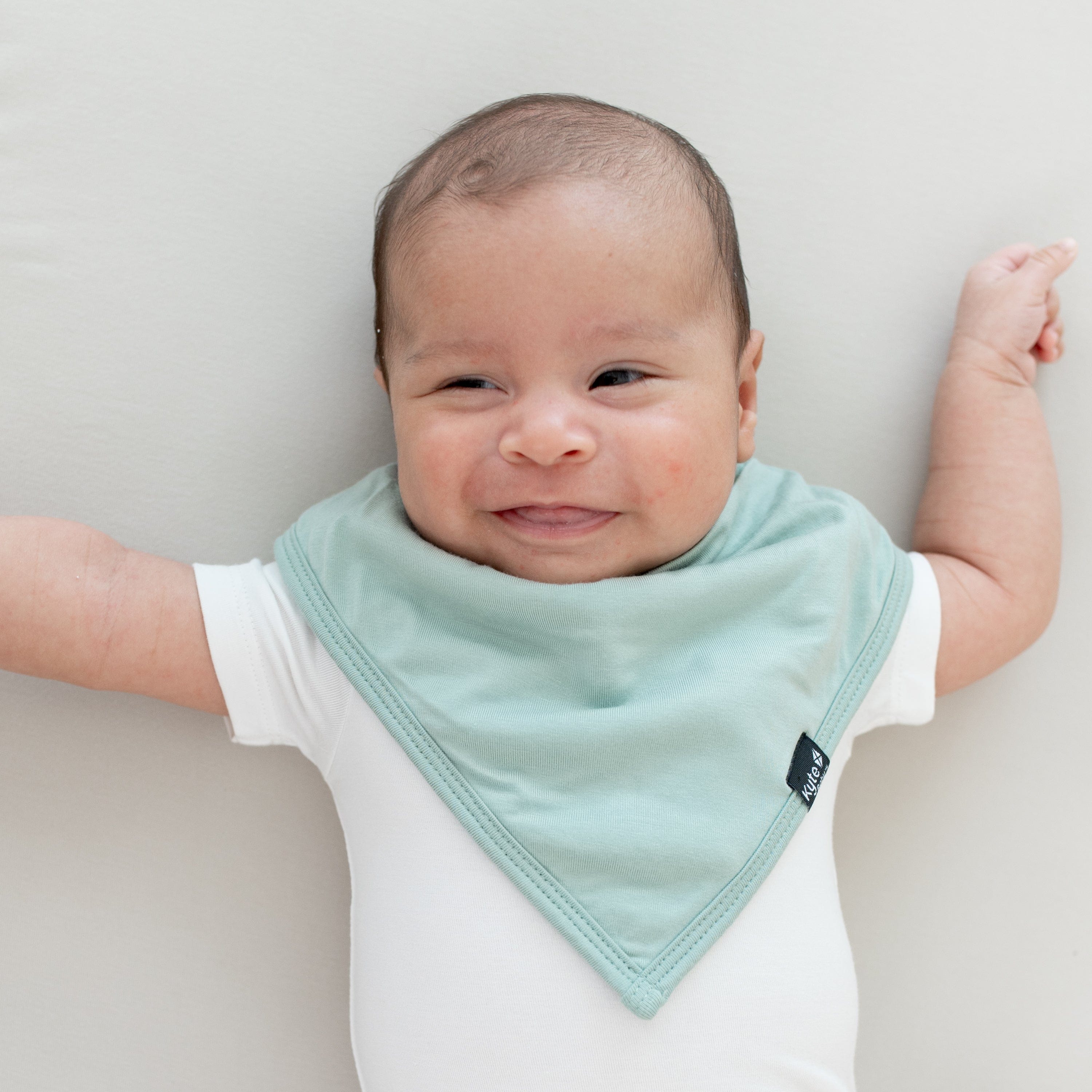 Smiling infant wearing the Kyte Baby Bib Sage and Short Sleeve Bodysuit in Cloud