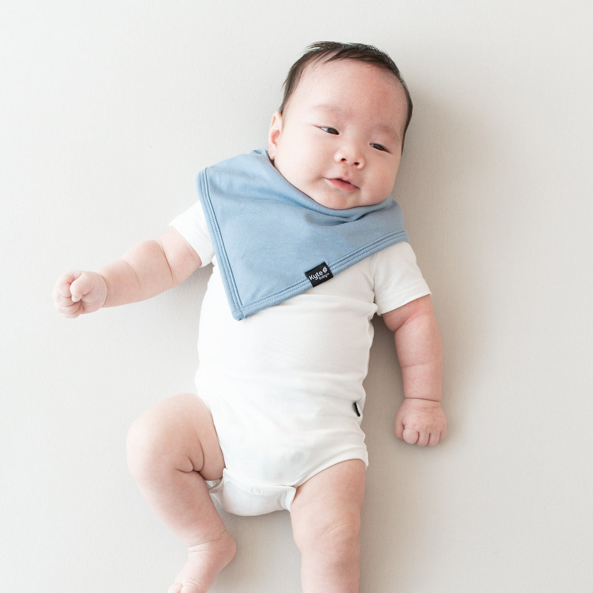 Baby laying on an oat surface while wearing a Bib in Slate