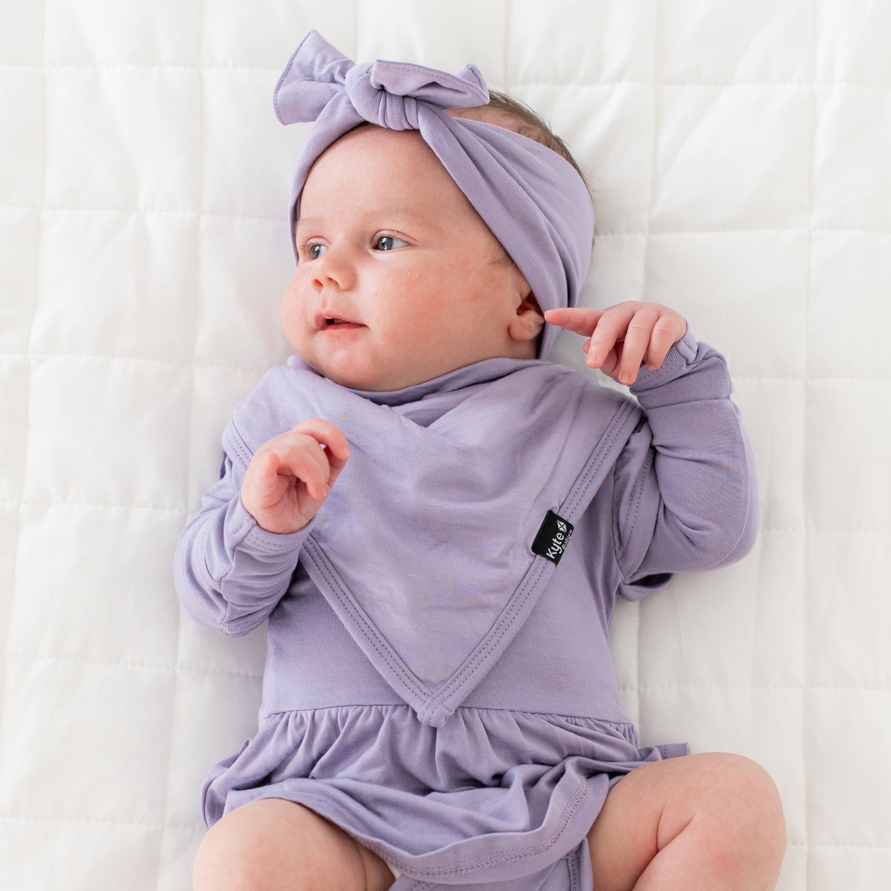 Baby wearing a bib in Taro with matching Twirl Bodsyuit and Bow