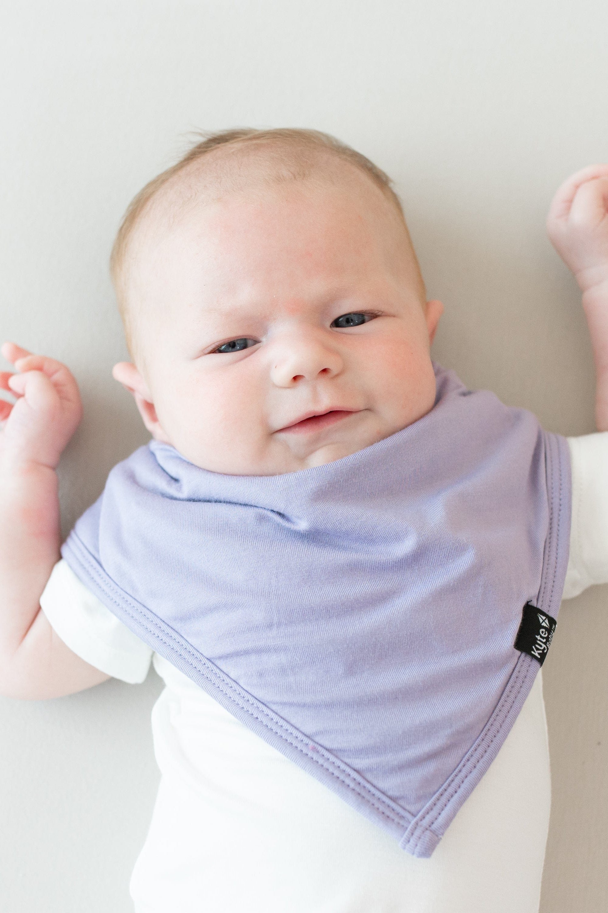 Baby modeling the Bib in Taro and Short Sleeve Bodysuit in Cloud