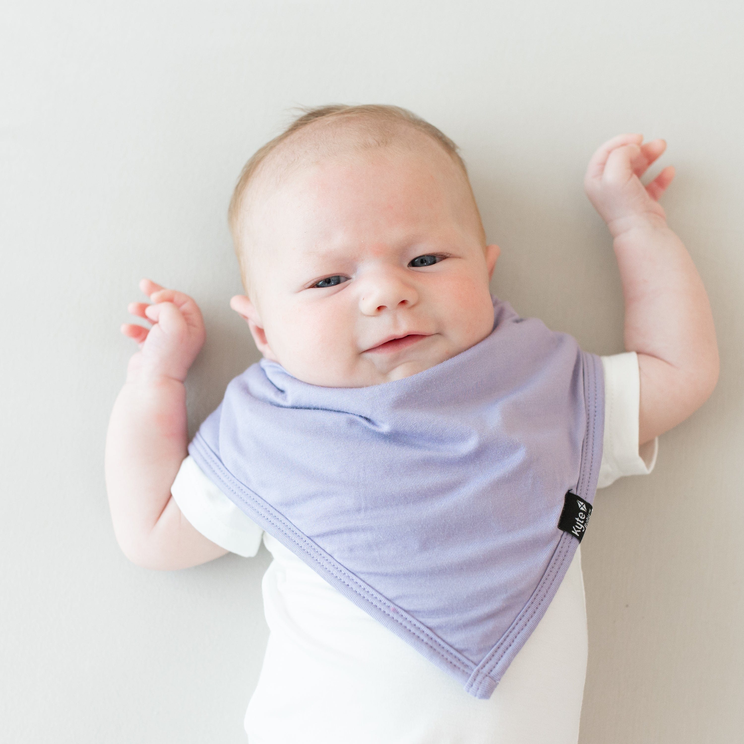 Baby modeling the Bib in Taro and Short Sleeve Bodysuit in Cloud