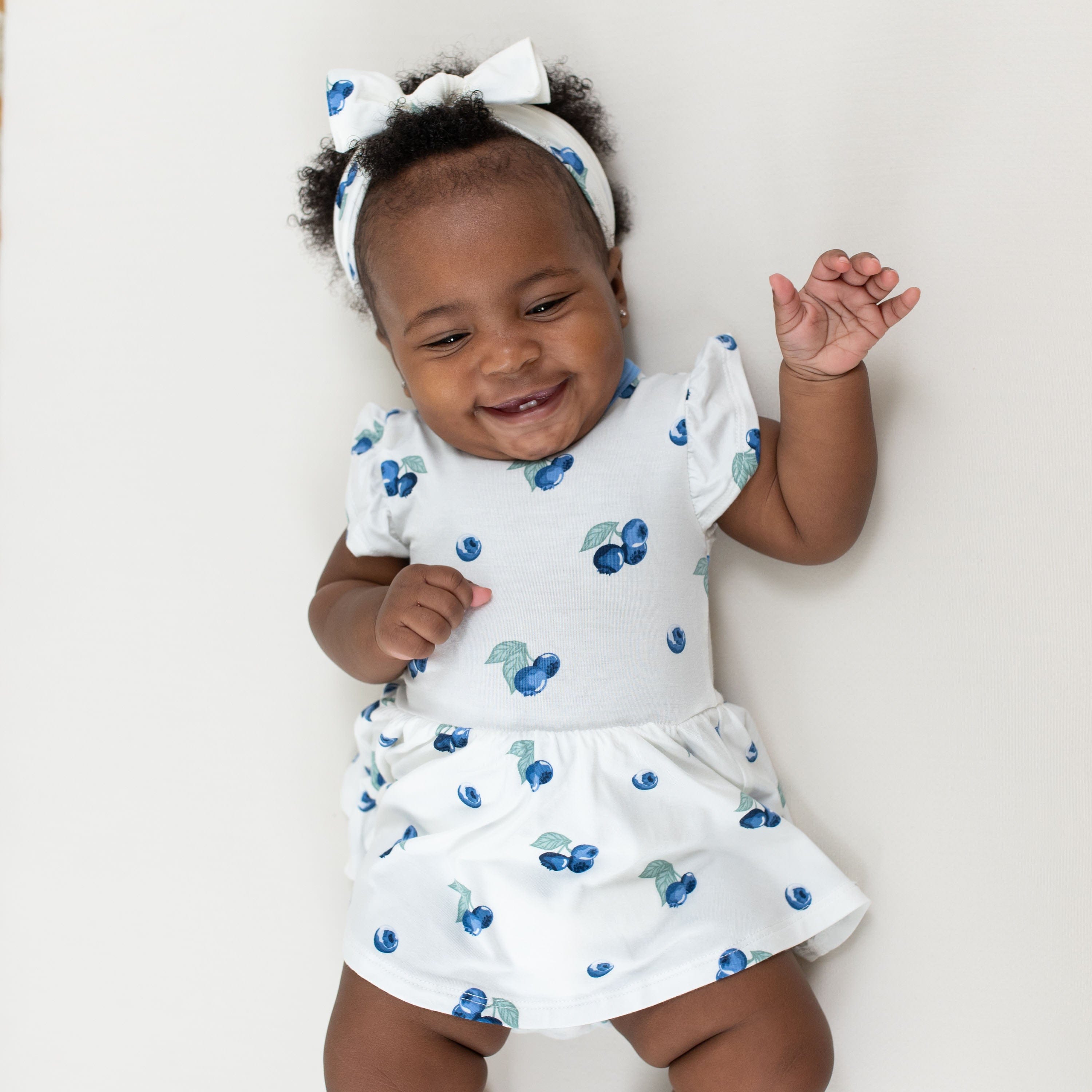 Baby wearing Twirl Bodysuit Dress in Blueberry with matching bow headband