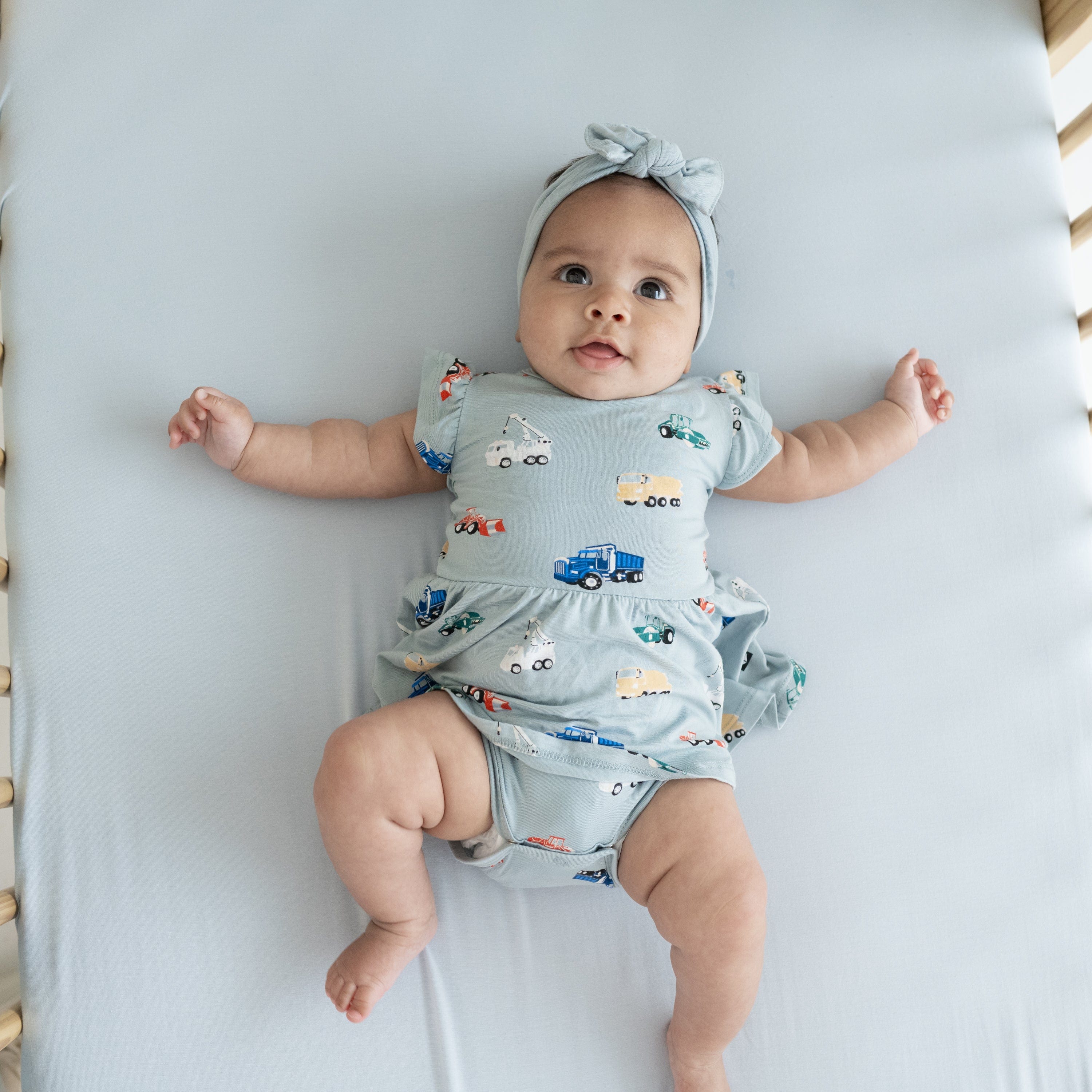 Baby wearing Twirl Bodysuit Dress in Construction with matching blue bow headband