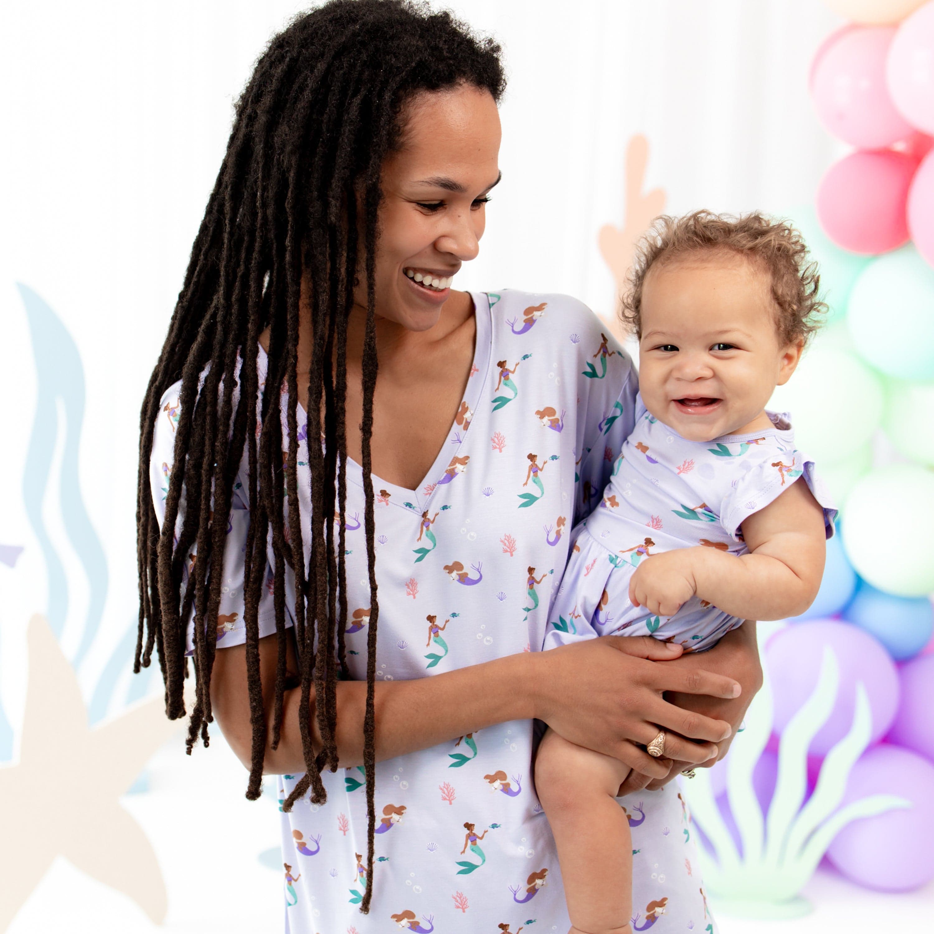 Mom holding Infant wearing Kyte Baby Twirl Bodysuit Dress with flutter sleeves in Mermaid