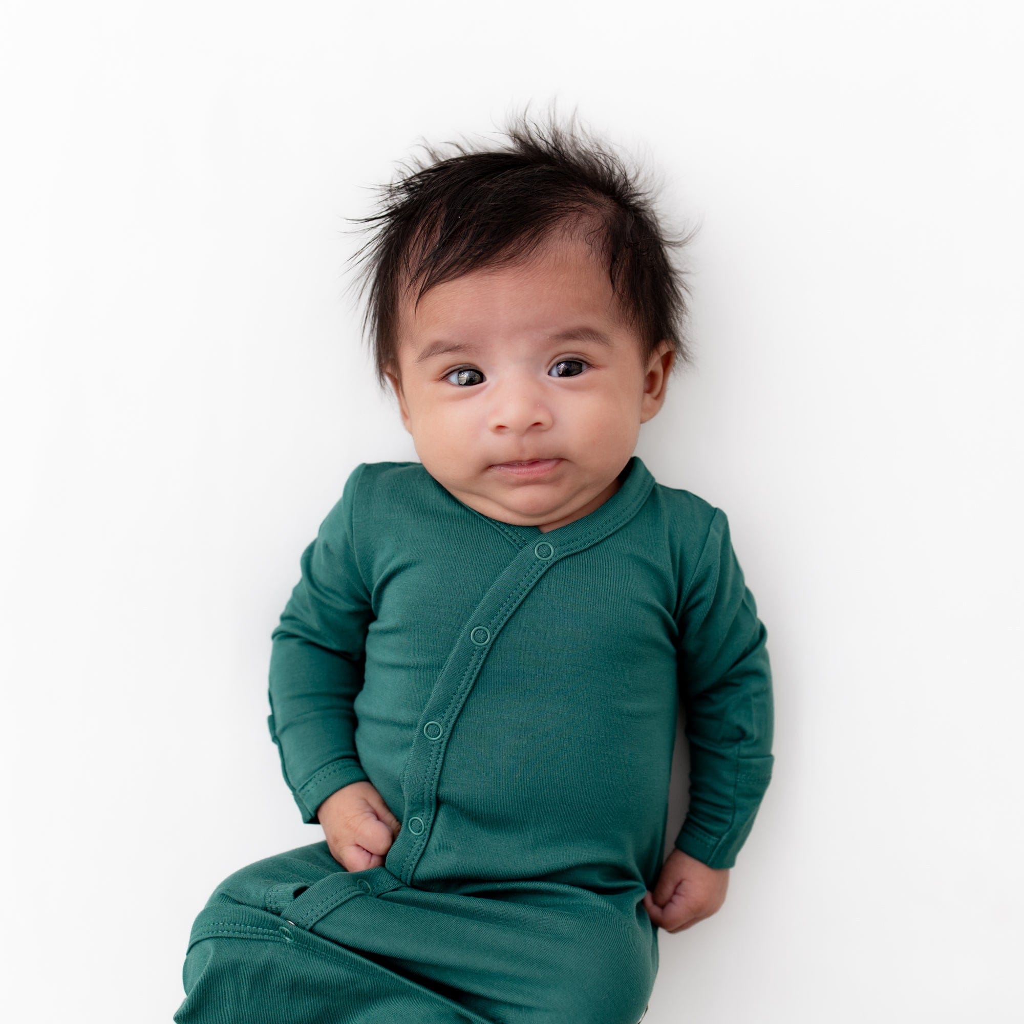 Infant laying on a white surface while wearing Kyte Baby Snap Bundler in Emerald