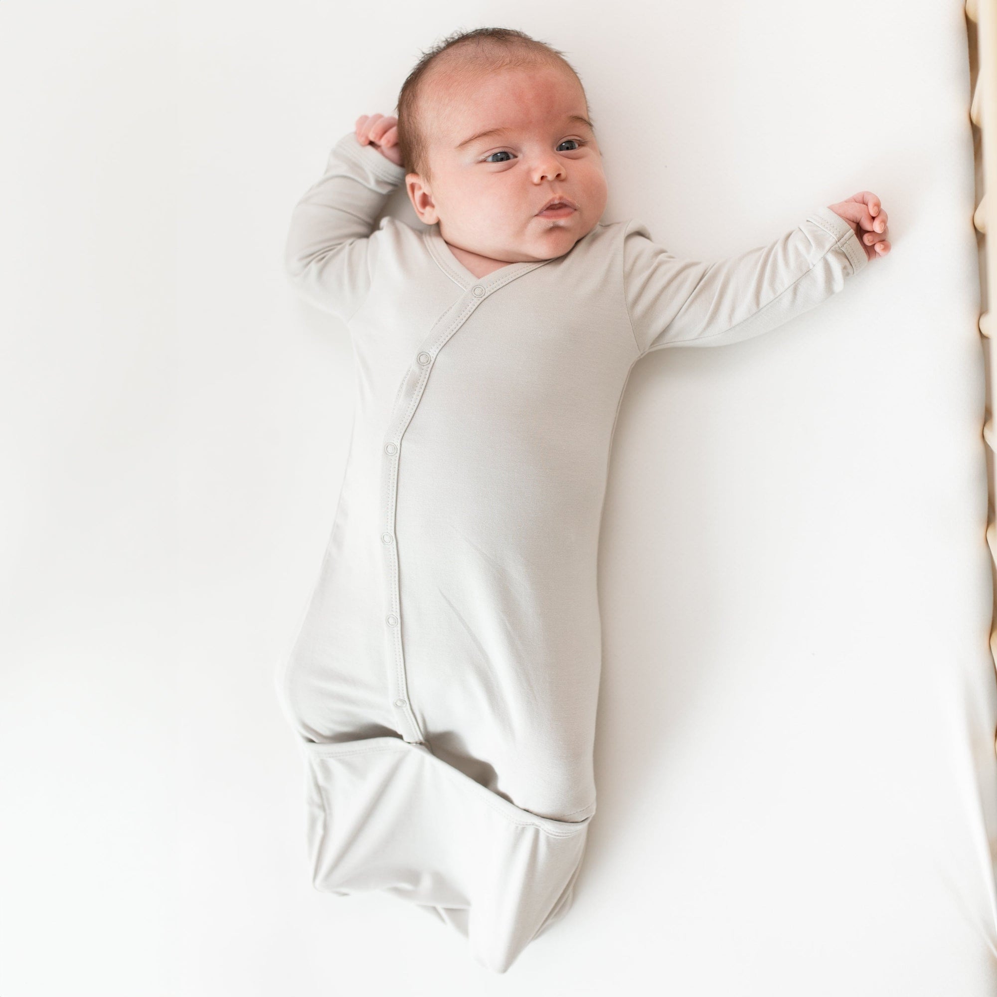 Newborn laying in crib while wearing the Kyte Baby Bundler in Oat