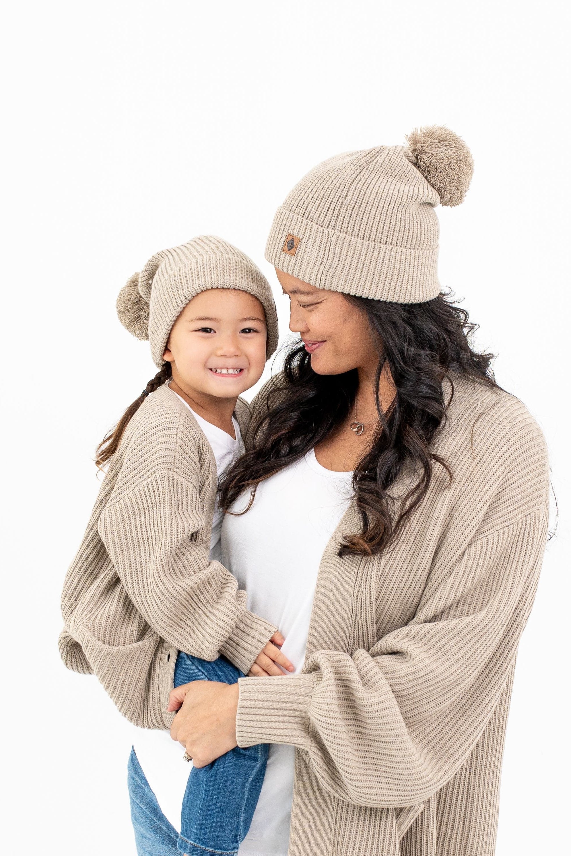 Mom and child wearing matching Kyte Baby Chunky Oversized Cardigan and Pom Beanies in Almond