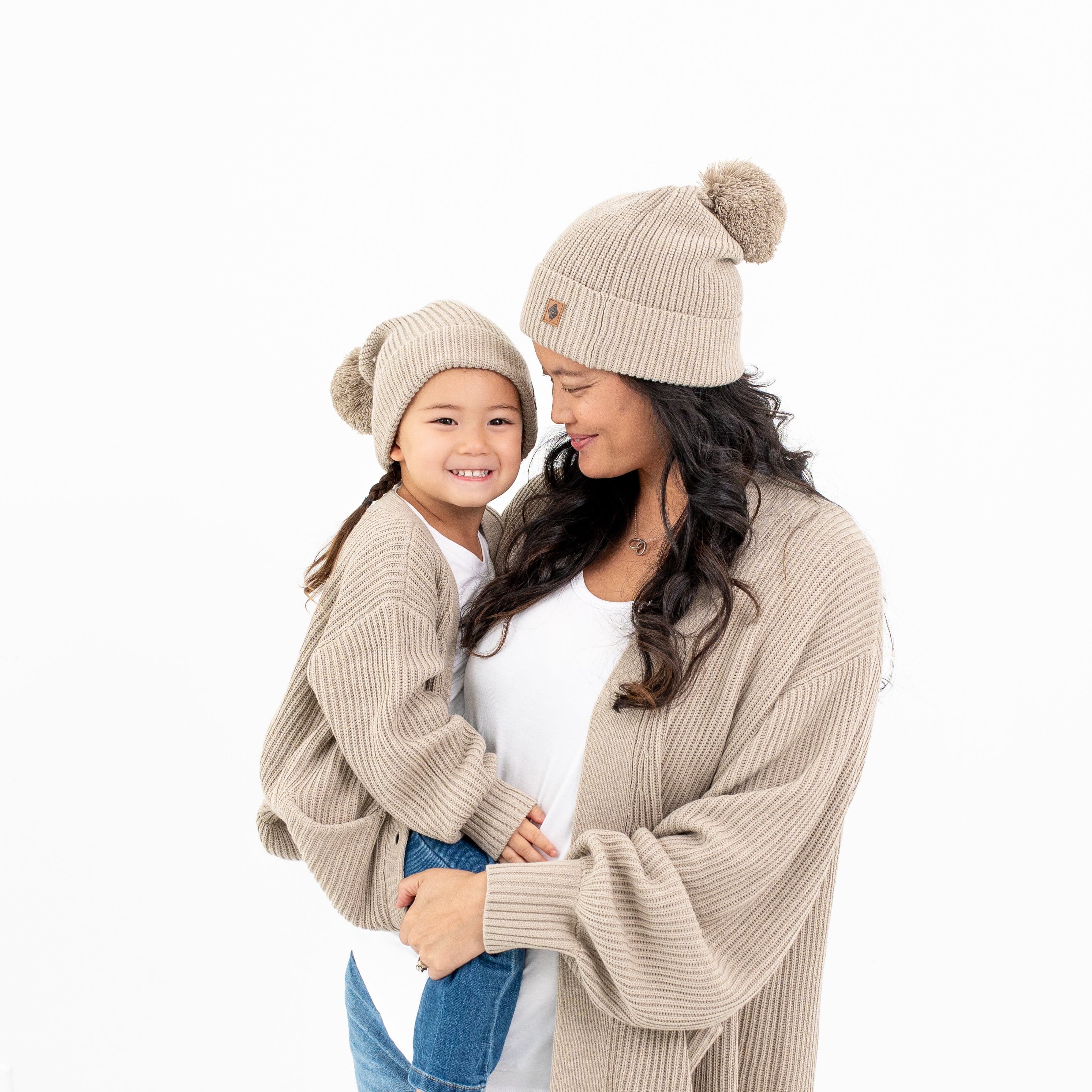Mom and child wearing matching Kyte Baby Chunky Oversized Cardigan and Pom Beanies in Almond