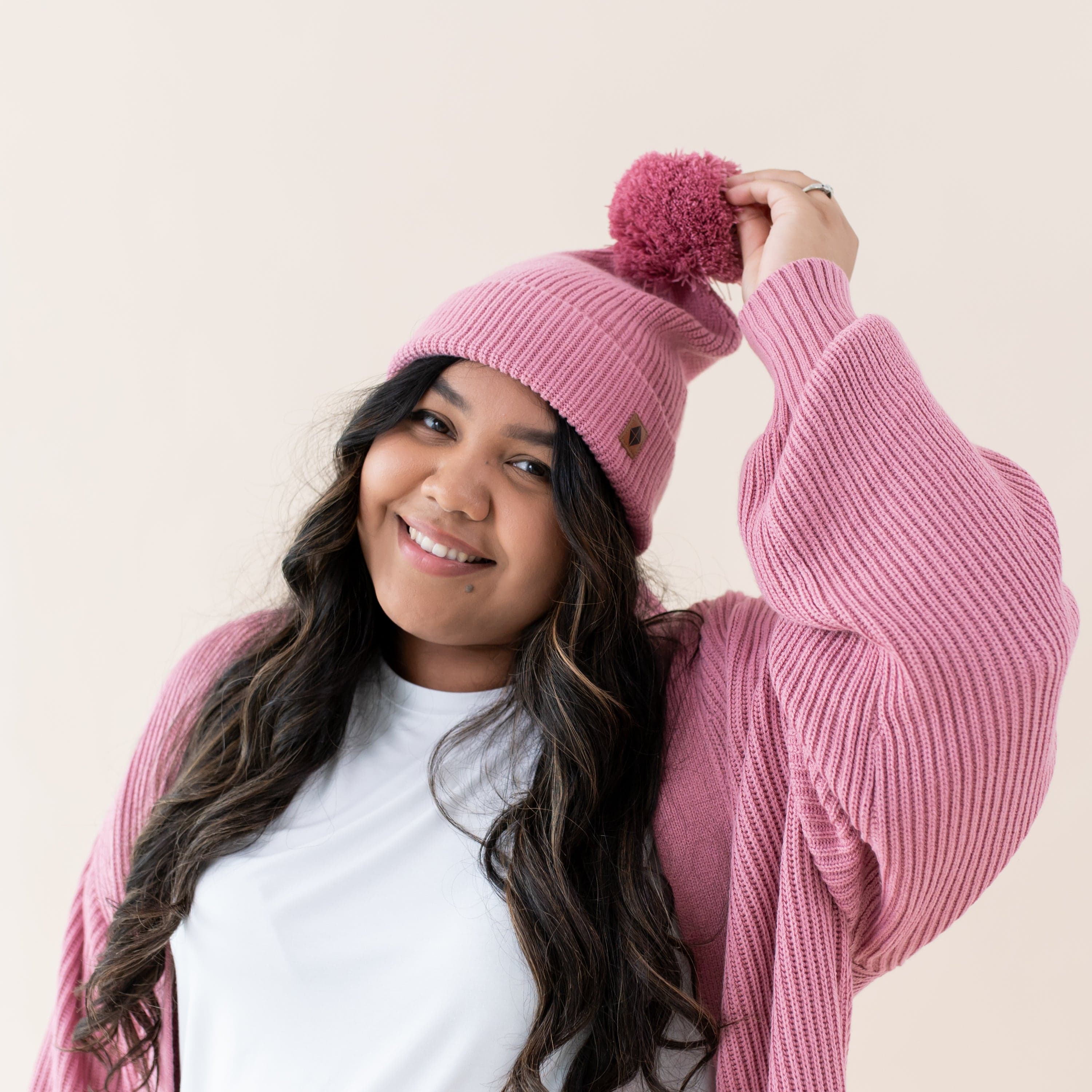 Woman wearing soft and stretch Kyte Baby Chunky Knit Adult Pom Beanie in Apple Blossom