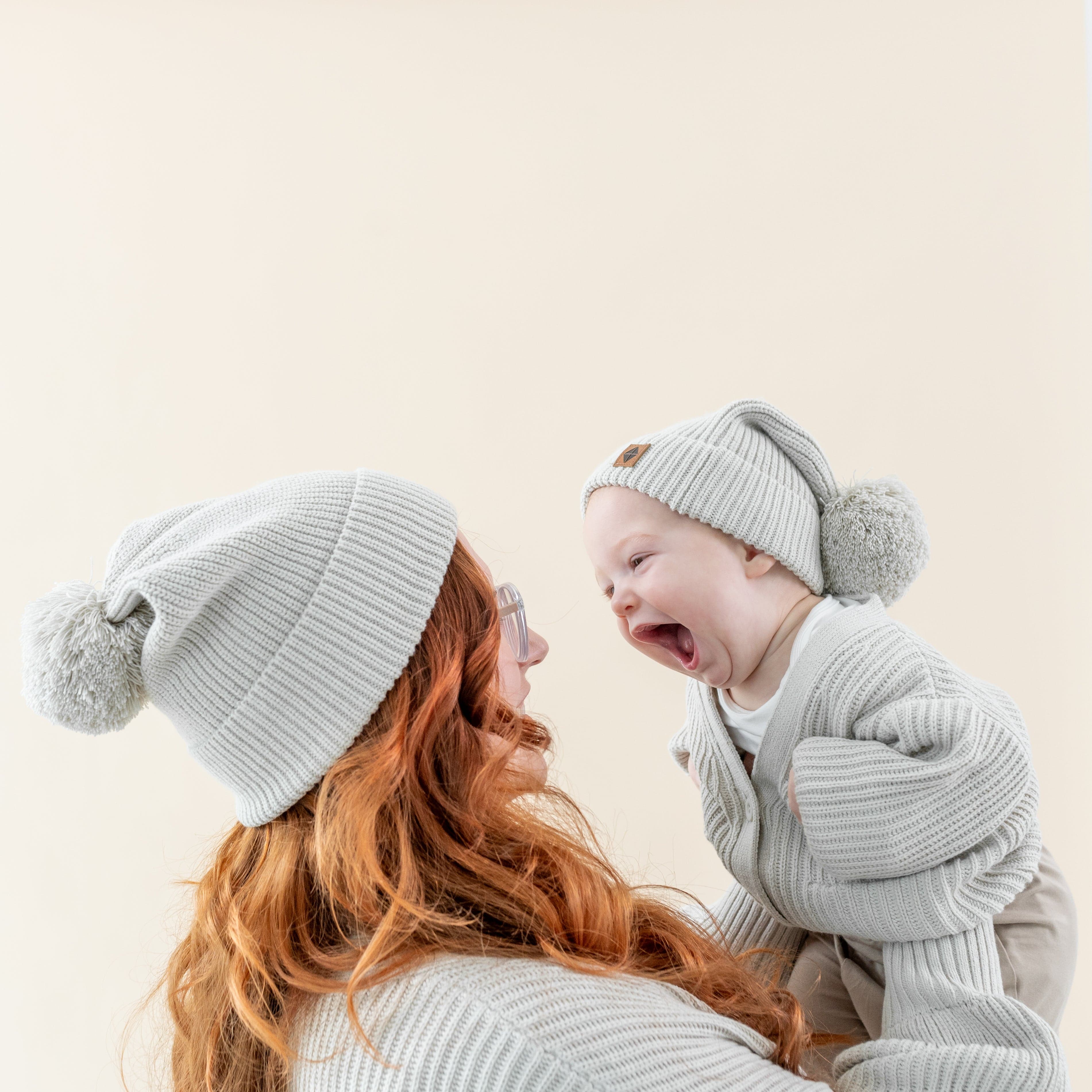 Mom and child wearing matching soft and stretchy Kyte Baby Chunky Knit Pom Beanies in Oat