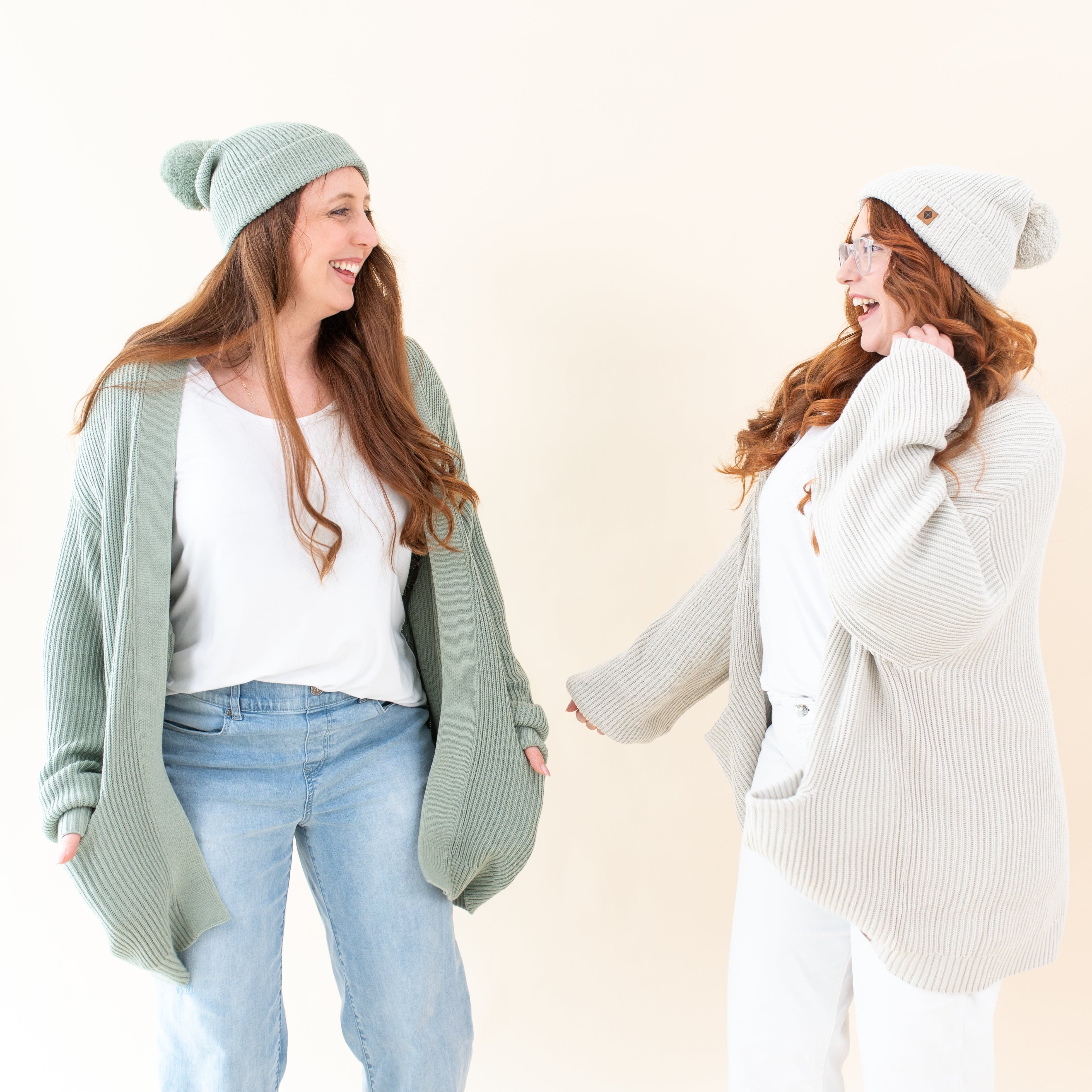 Women wearing Kyte Baby Chunky Knit Adult Pom Beanies and Cardigans in Thyme and Oat