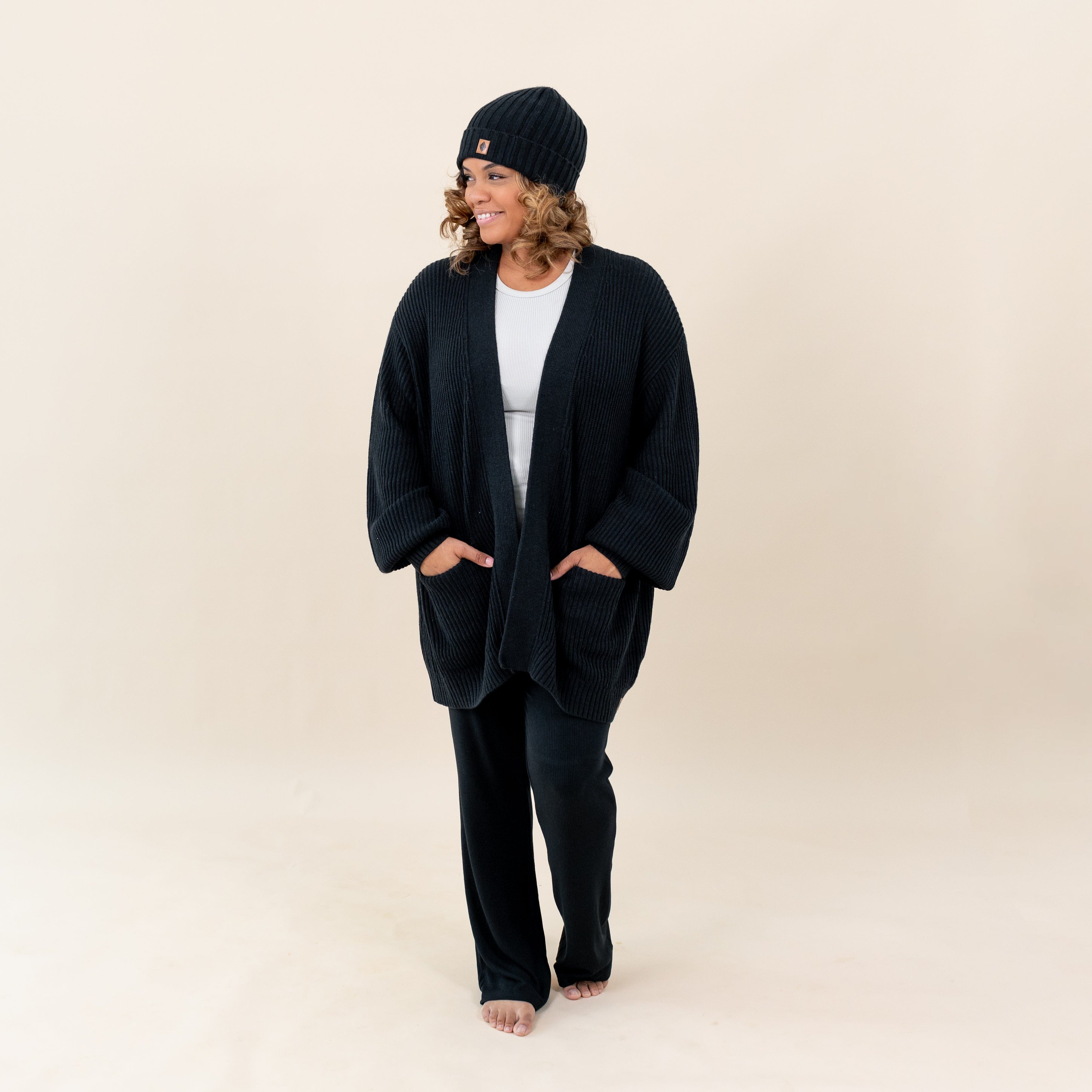 Woman wearing Kyte Baby Chunky Knit Oversized Cardigan with Front Pockets and Ribbed Beanie in Midnight