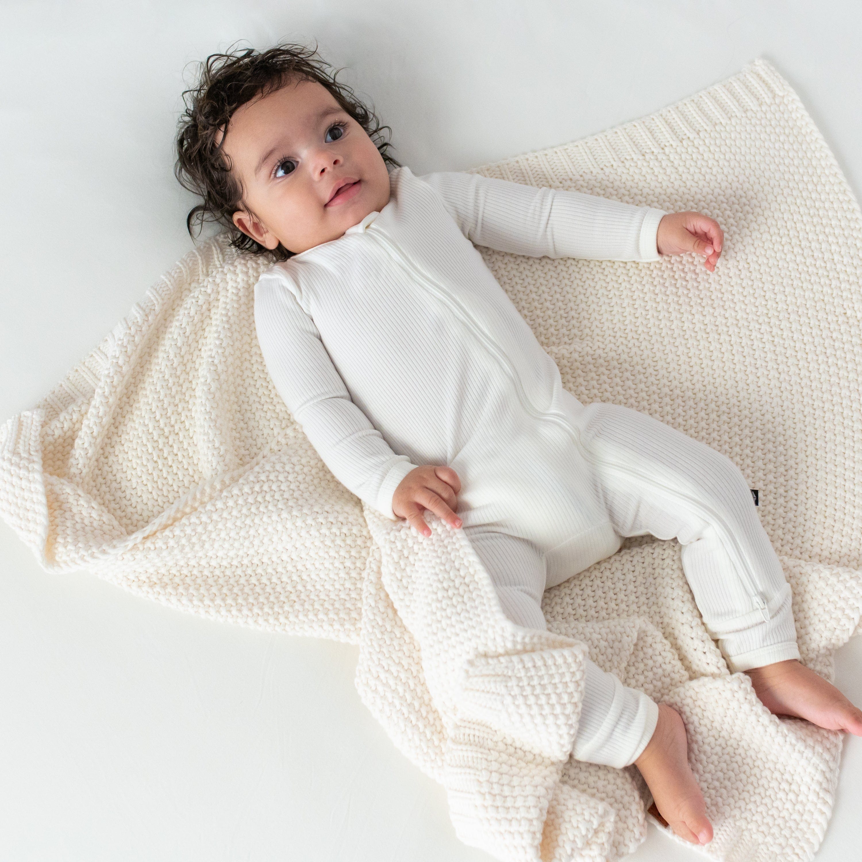 Infant laying on Kyte Baby Chunky Knit Baby Blanket in Cloud